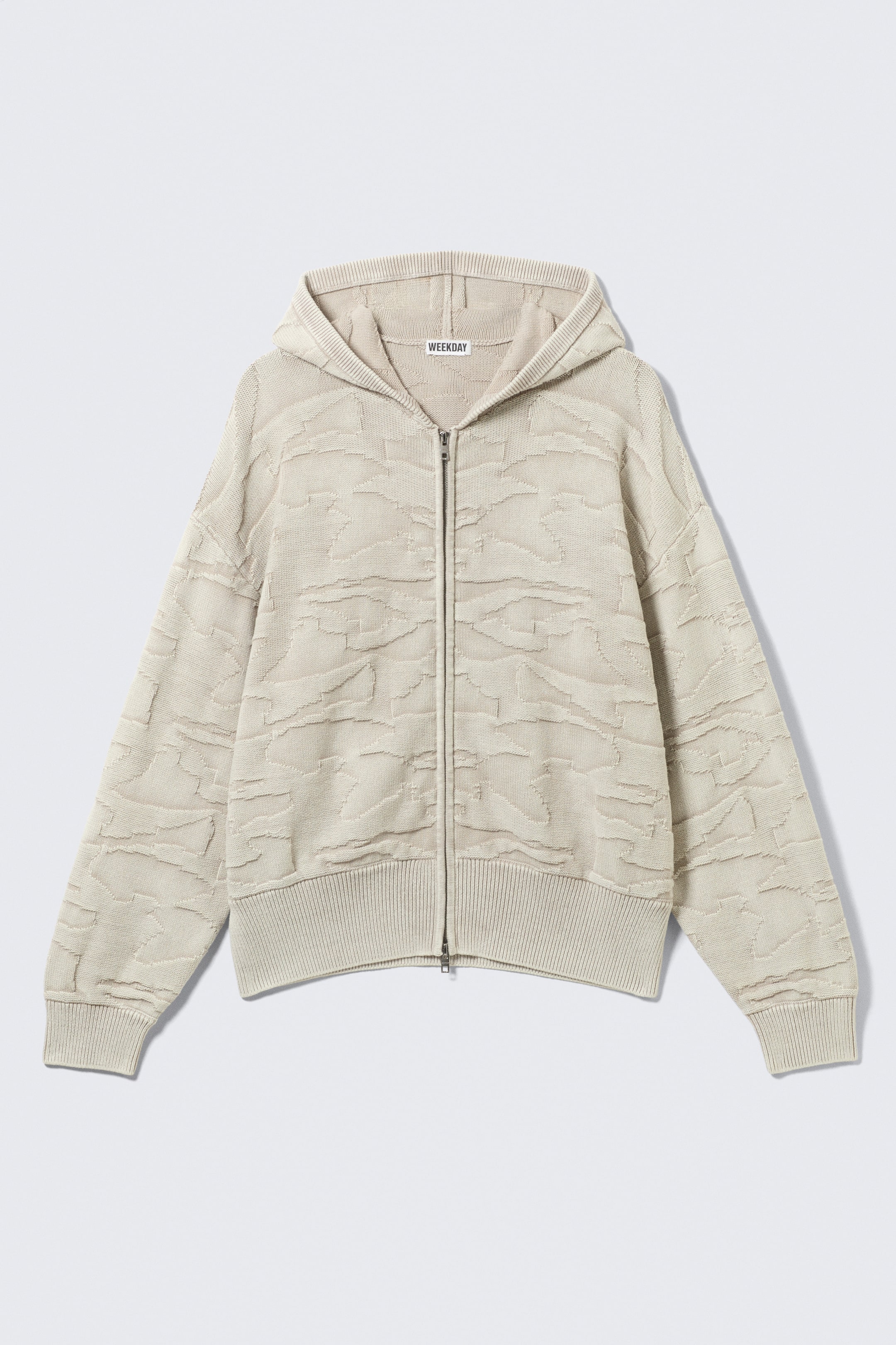 Ver imagen más grande: Un cárdigan con capucha de color beige claro presenta su parte frontal, con un patrón abstracto y texturizado a lo largo de su cuerpo y mangas. Incluye un cierre de cremallera de longitud completa, puños acanalados, un dobladillo acanalado y una etiqueta de la marca "WEEKDAY" en el cuello interior.