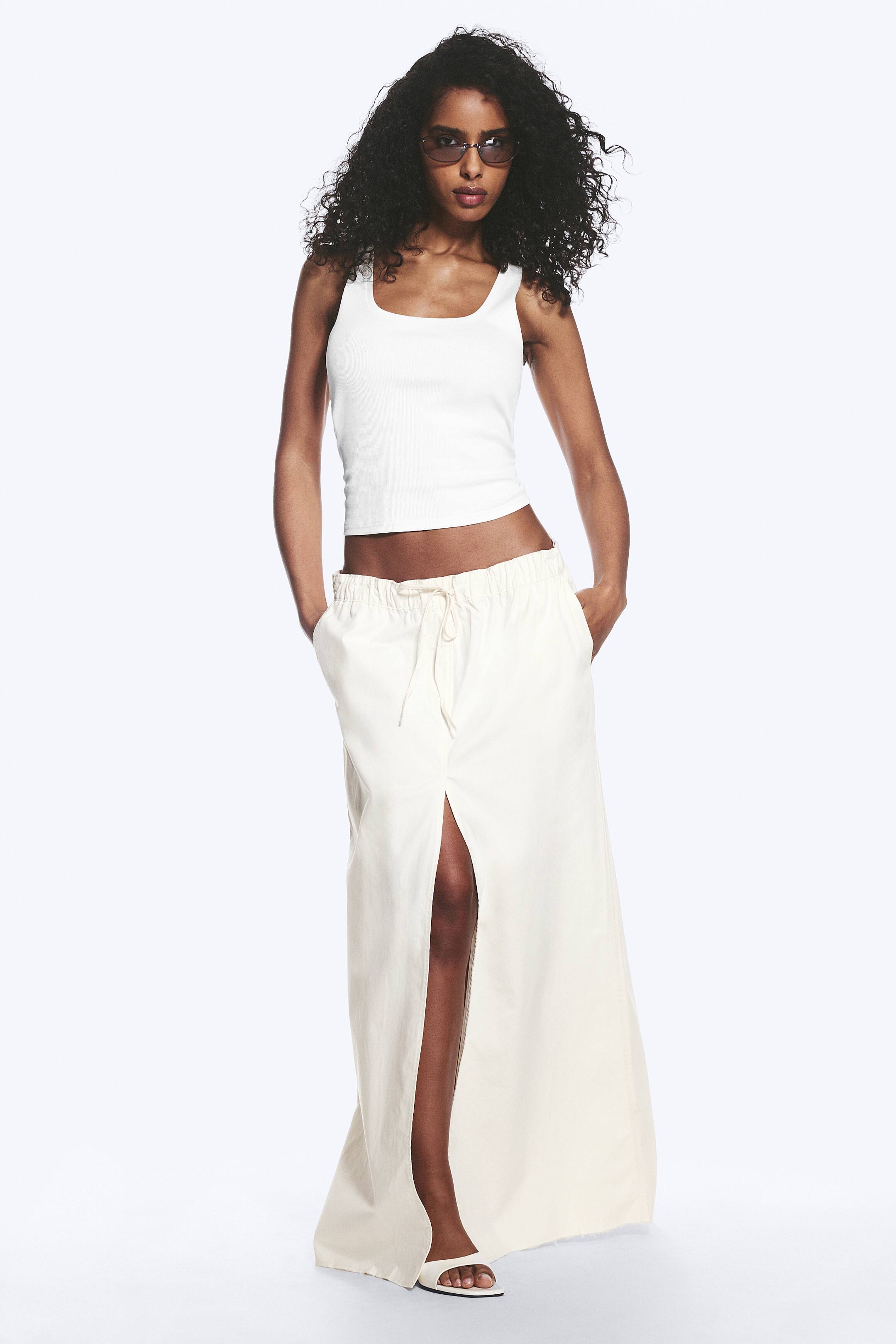 Größeres Bild ansehen: Ein weißes, geripptes Crop-Top mit quadratischem Ausschnitt und breiten Trägern. Ein cremefarbener Maxirock mit elastischem Kordelzugbund, Seitentaschen und einem hohen Frontschlitz.