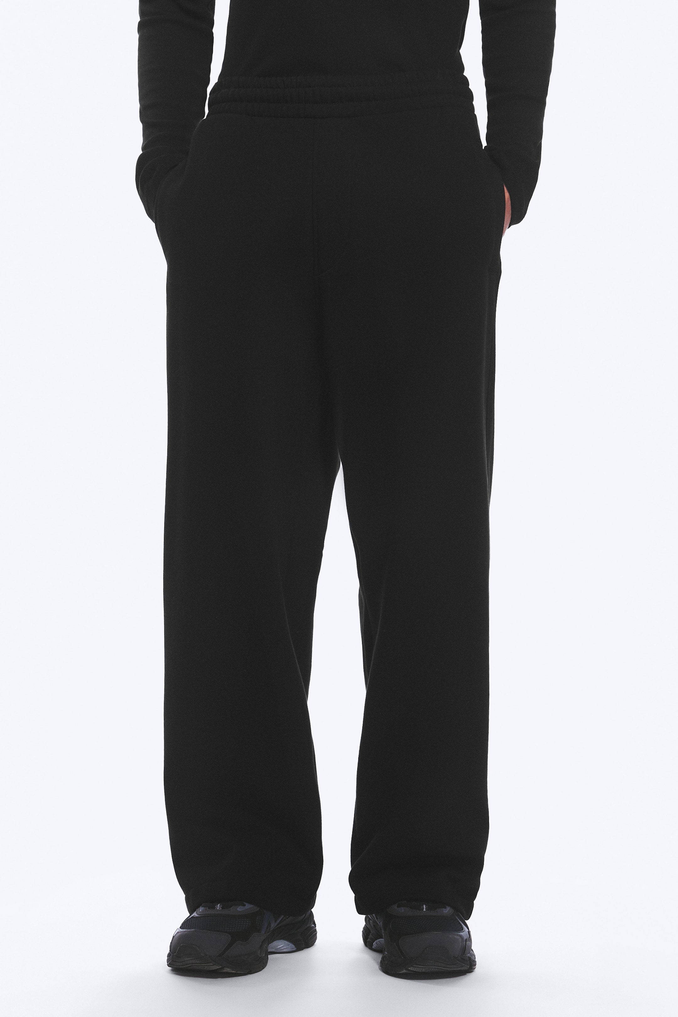 Agrandir l'image: Pantalon noir à coupe ample présenté de face, avec une taille élastiquée et des poches latérales où reposent les mains.