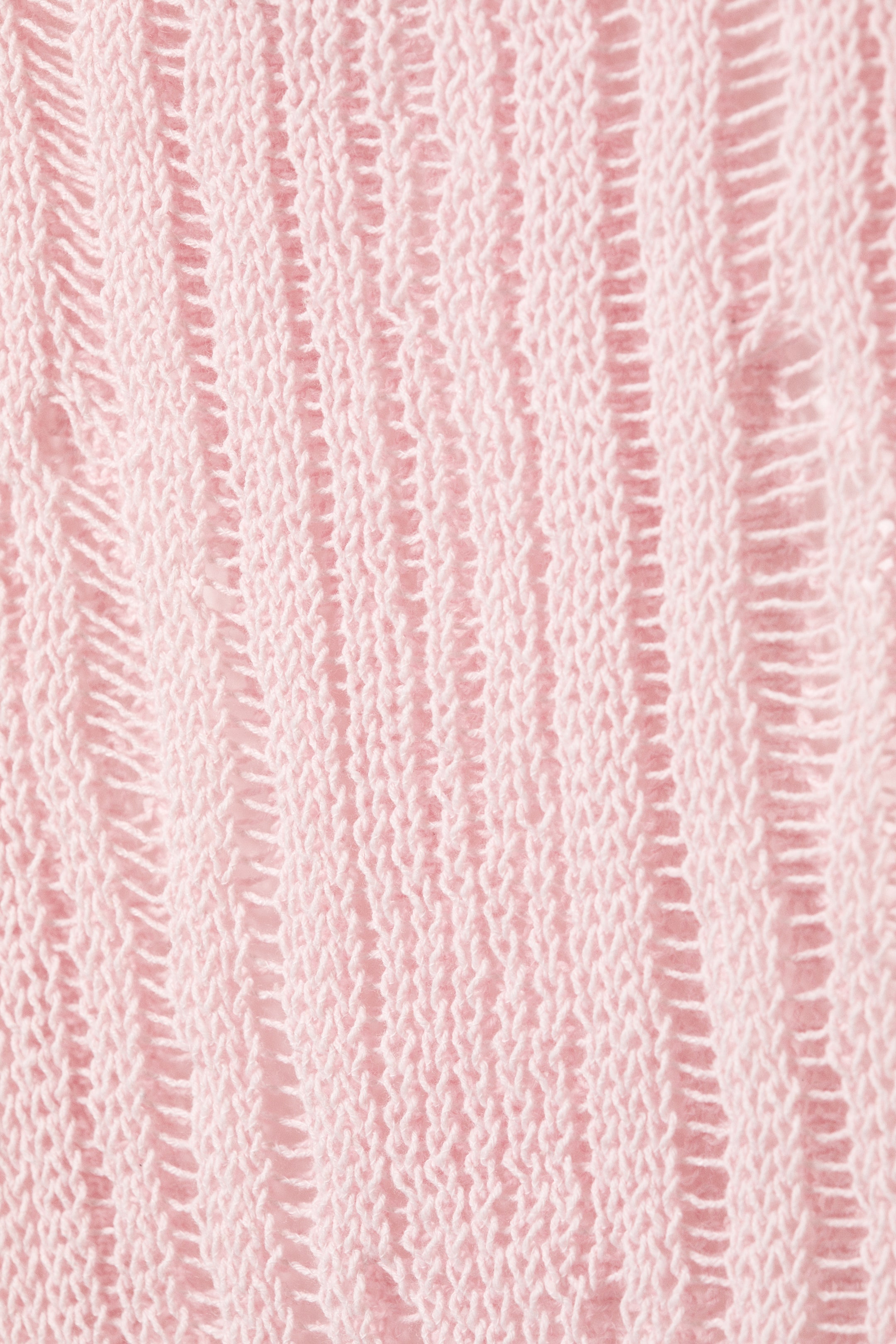 Vezi imaginea mai mare: Un maieu roz tricotat prezintă un model texturat, cu tricot vertical, afișând benzi verticale alternante de tricot solid și cusături deschise, asemănătoare unei scări.