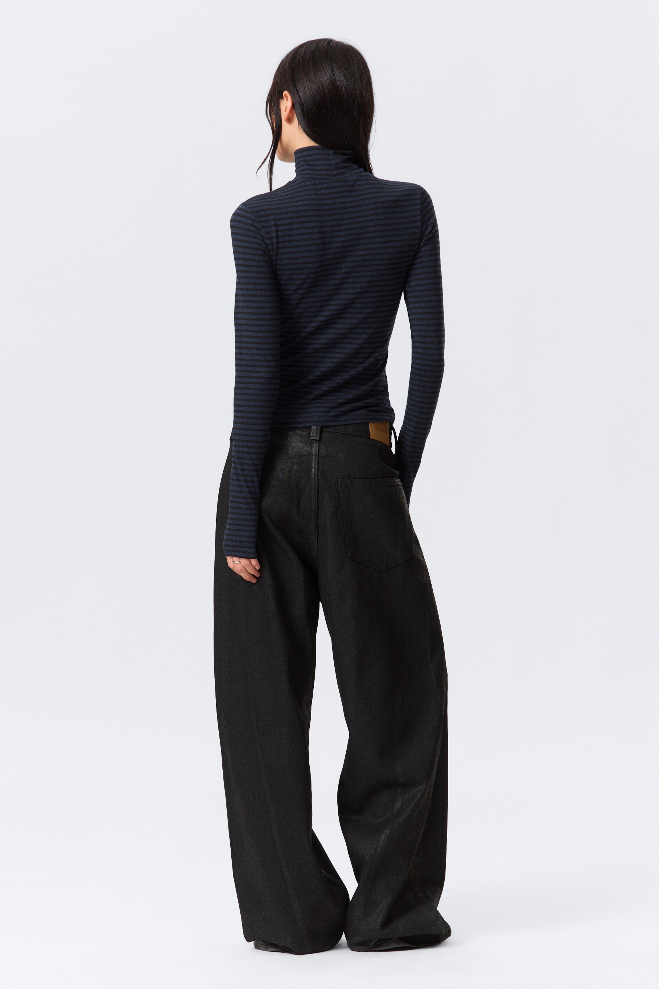 Grotere afbeelding bekijken: De zwarte wijde broek wordt van achteren gepresenteerd, met een subtiele glans, een hoge taille en wijde, lange pijpen die bij de enkels samenkomen. Twee grote opgestikte zakken zijn zichtbaar aan de achterkant, samen met een klein bruin label op de rechter tailleband.