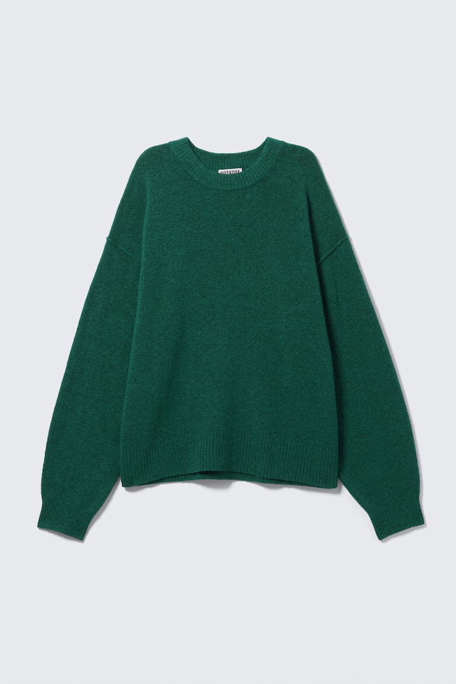 A dark green sweater is lying flat, showcasing a fuzzy texture and a relaxed fit. It is featuring a ribbed crew neck, long sleeves with ribbed cuffs, and a ribbed hem. - 1