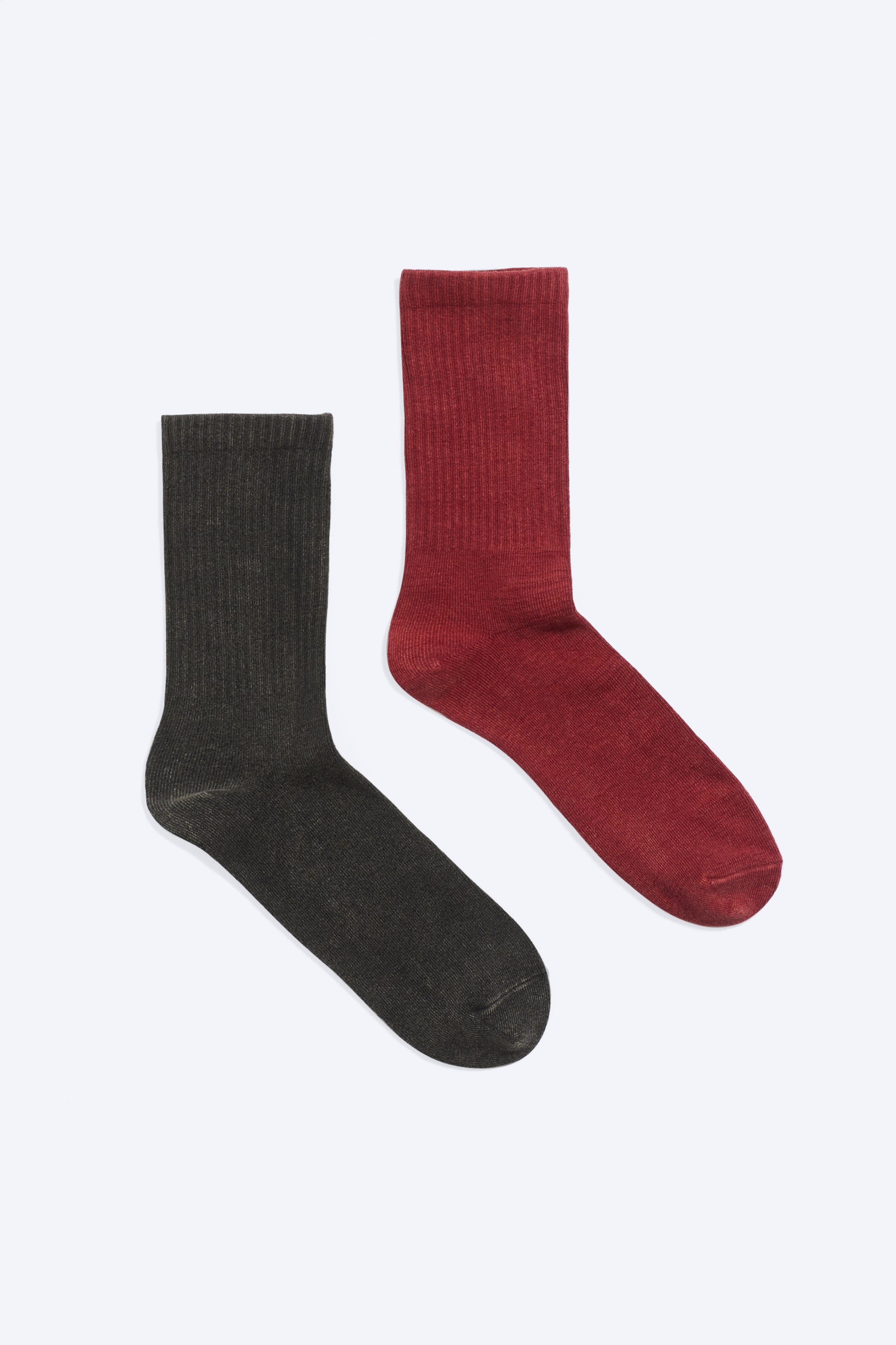 View larger image: Two crew socks are laid flat, showing their front sides. One dark grey sock and one dark red sock are displayed with ribbed shafts, cuffs, and a washed finish, with their toes pointing downwards.