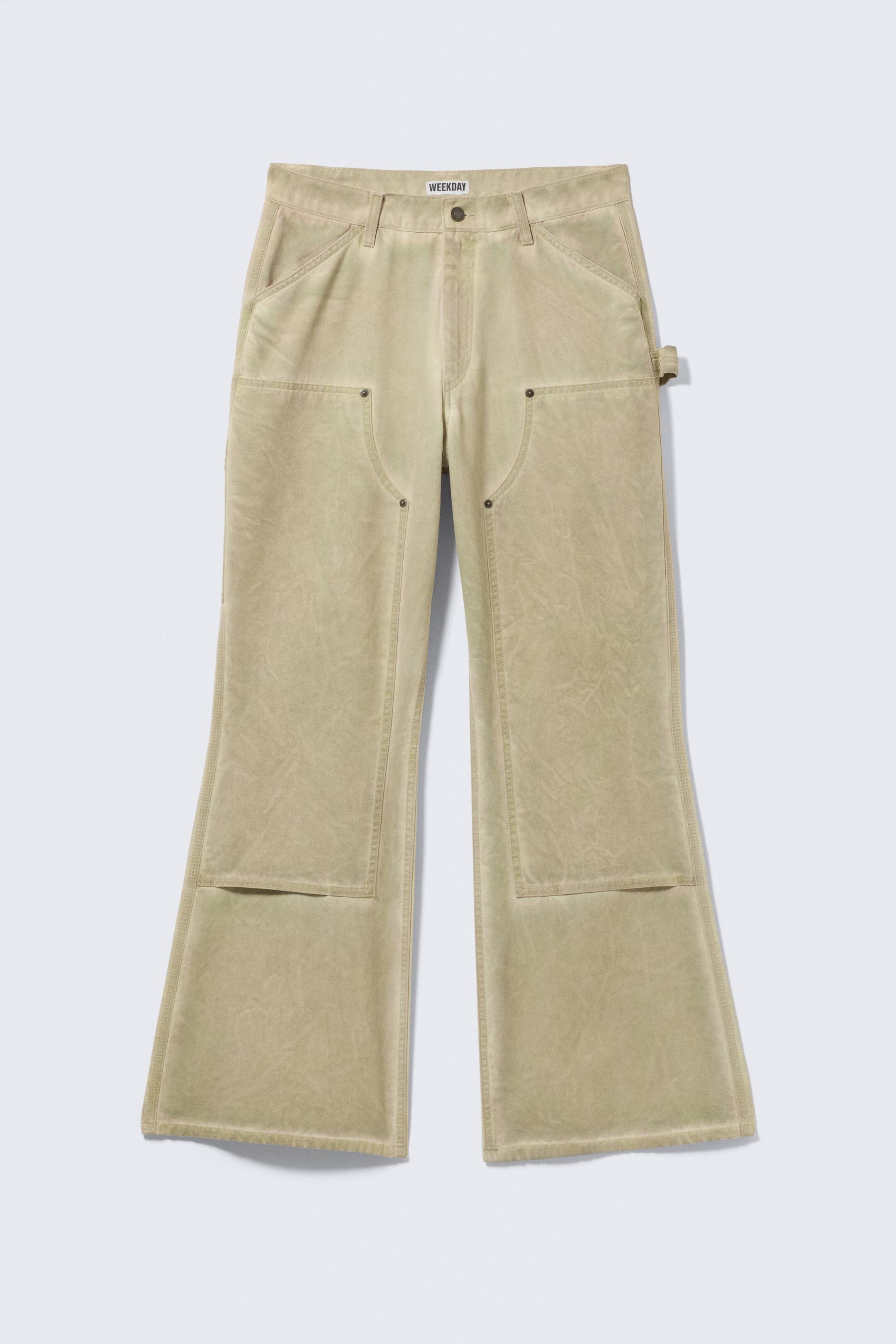 View larger image: The FRONT of a pair of light olive-green utility trousers showcases a washed-out texture. They feature a standard waistband with belt loops, a button and zip fastening, front curved pockets with metal rivets, a hammer loop on the right hip, and large rectangular panels on the front of the legs, flaring out into a wide leg opening.