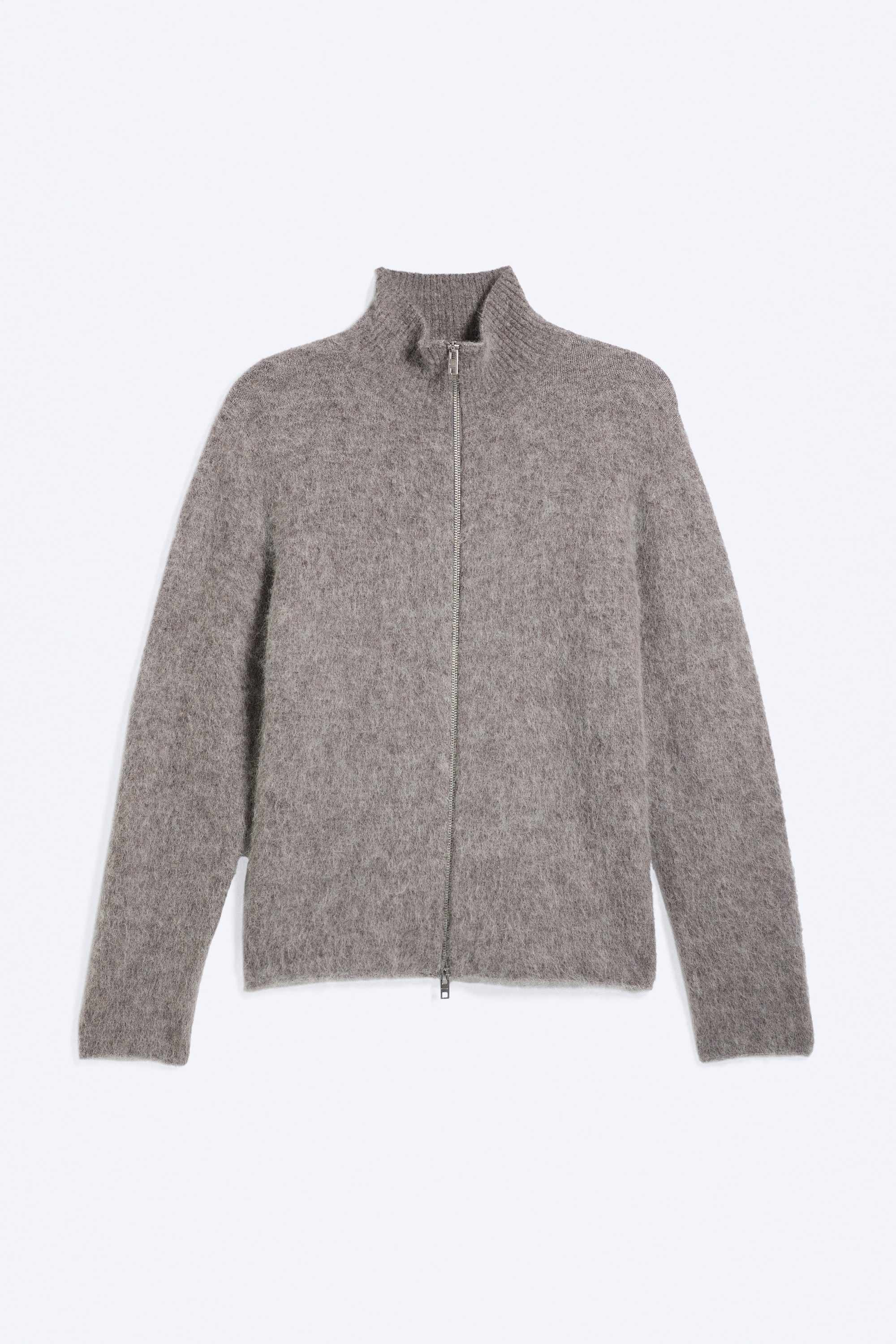 En blød, grå strikcardigan i en afslappet pasform bæres af modellen over en hvid, stribet skjorte med knapper og slidte blå jeans. Cardiganen har en delvist lynlåst tovejslukning foran, lange ærmer og ribkanter.