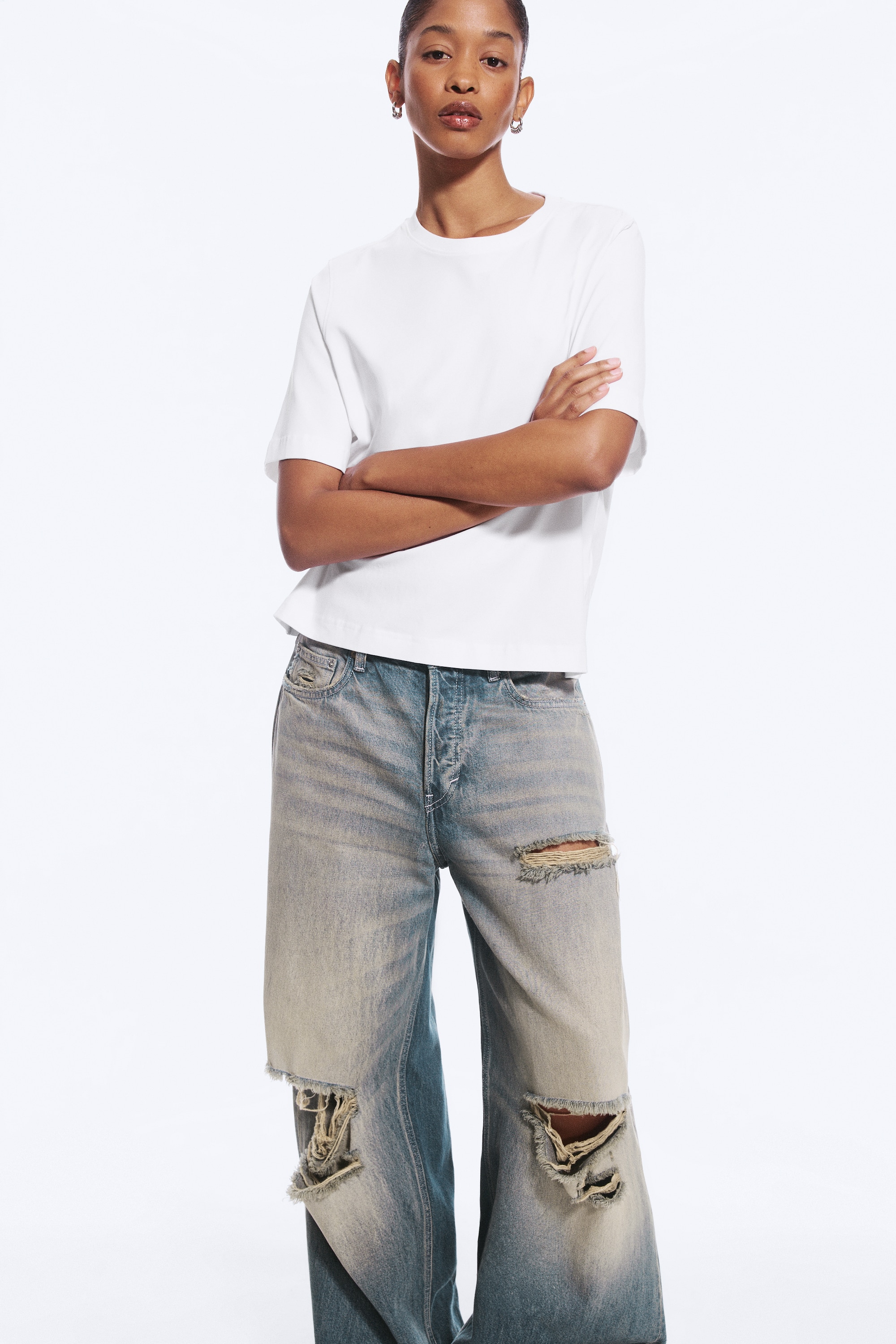 Een witte oversized t-shirt wordt van voren getoond, met een geribbelde ronde hals en ellebooglange mouwen. Het heeft een boxy vorm met een rechte zoom.