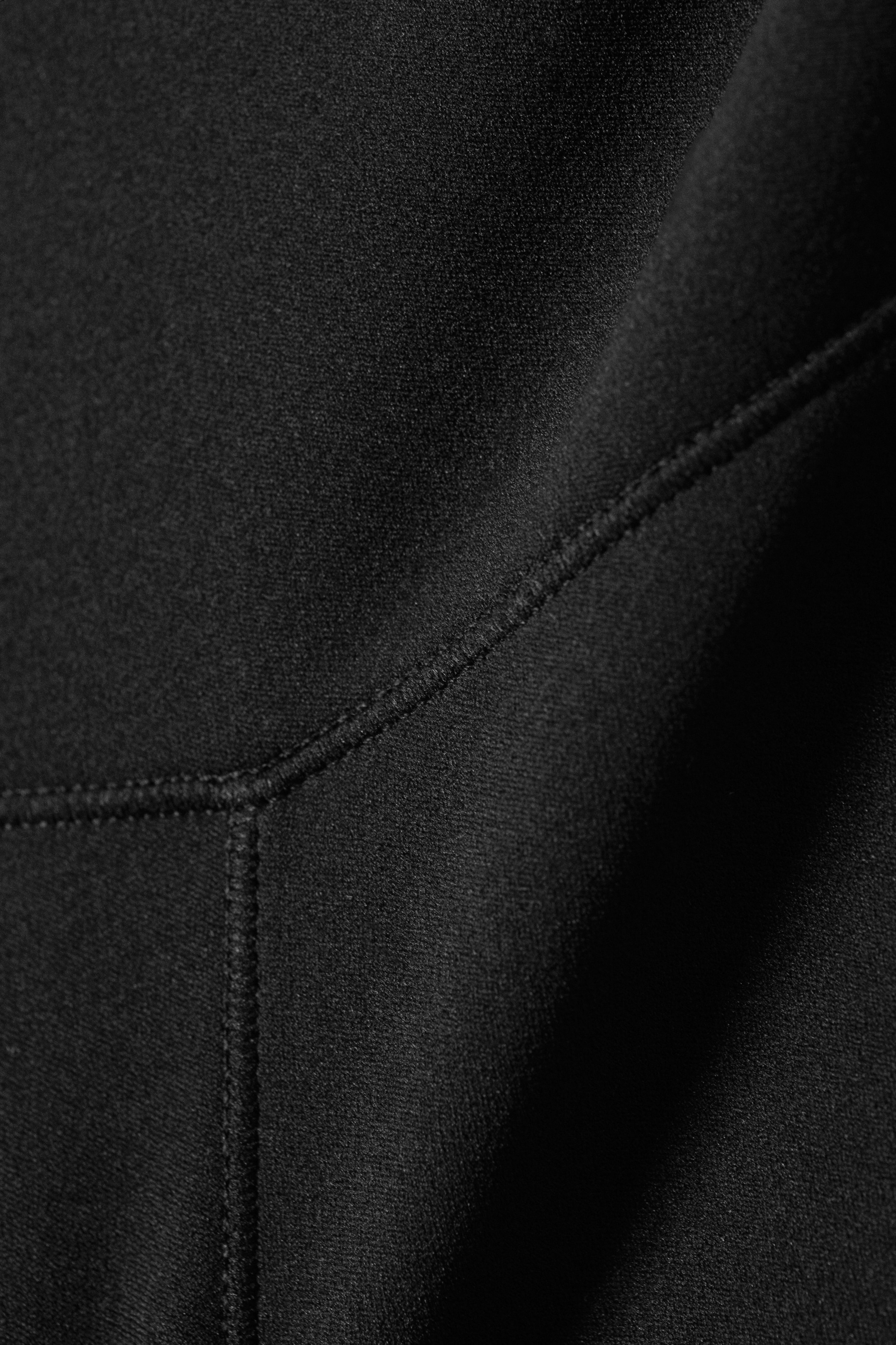 Agrandir l'image: Le tissu en maille noir présente des coutures flatlock noires proéminentes. Les coutures forment des coutures qui convergent en un point central, créant des panneaux distincts et des courbes subtiles dans le tissu.