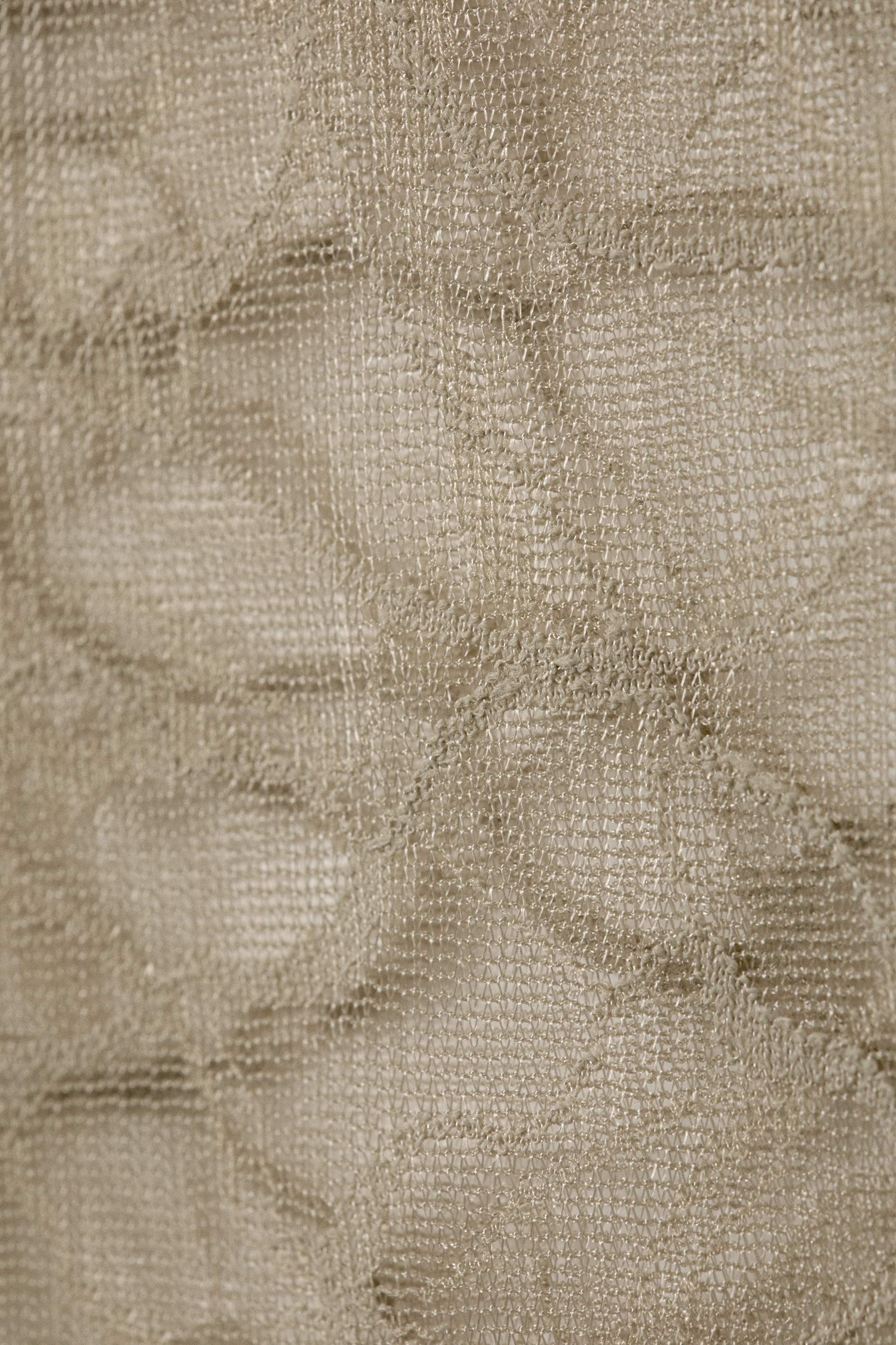 Grotere afbeelding bekijken: Een licht beige geweven materiaal toont een fijne, open-gaasstructuur. De stof heeft onregelmatige rimpels en subtiele plooien over het getextureerde oppervlak.