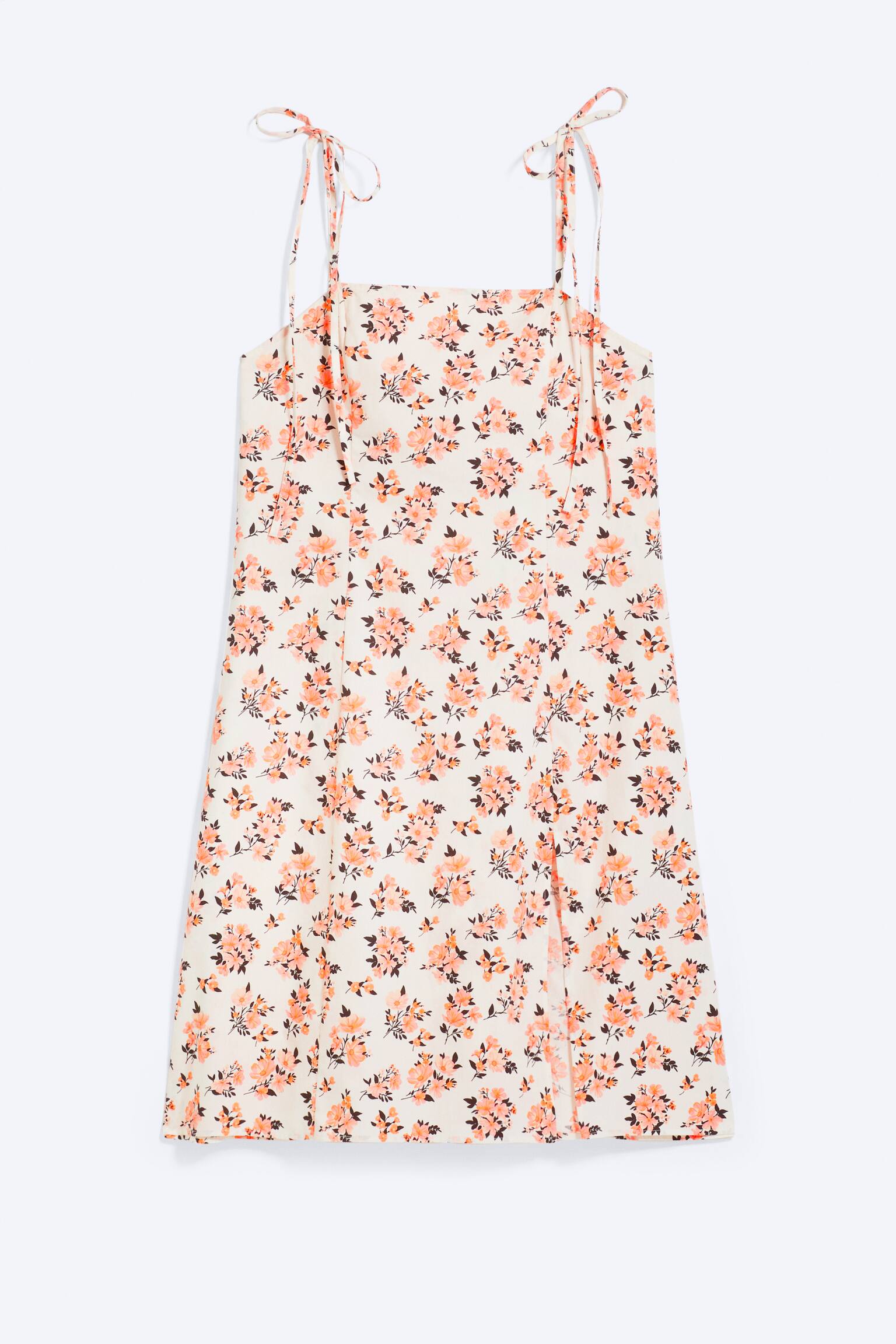 Een crèmekleurige bloemen mini-jurk wordt van voren getoond, met een vierkante halslijn, dunne zelfstrikkende schouderbandjes die in strikjes zijn gebonden, en een algeheel patroon van kleine perzik- en bruine bloemen, met een split aan de voorkant van het linkerbeen.