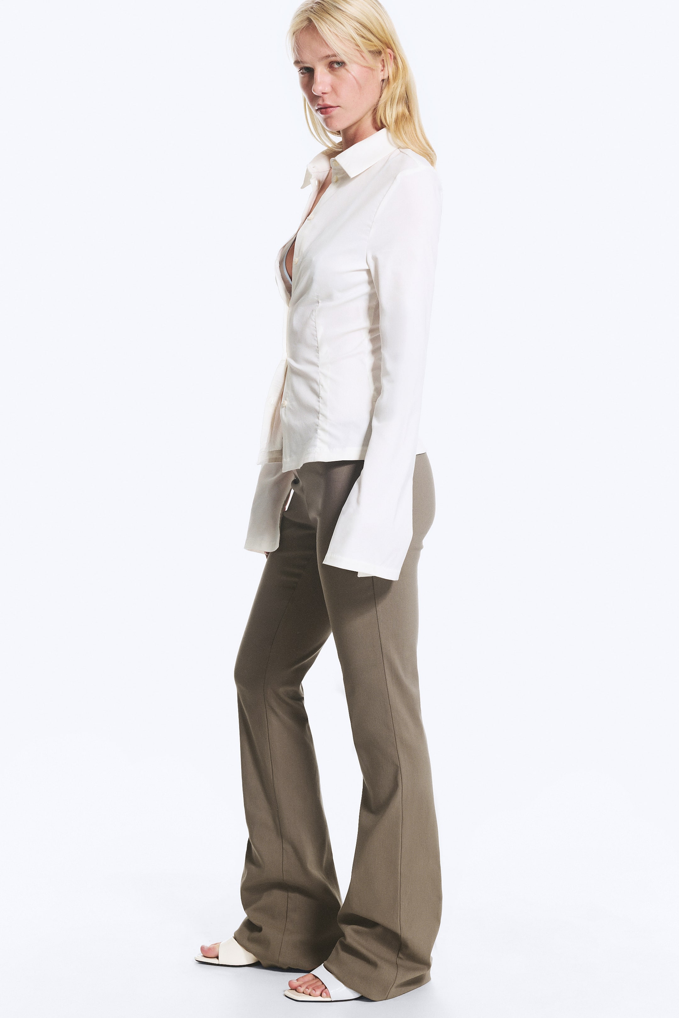 Agrandir l'image: Pantalon évasé vert kaki présenté sous un angle de côté-avant, avec une silhouette ajustée au niveau des hanches et des cuisses qui s'évase nettement à partir du genou. Une couture visible parcourt le centre de chaque jambe.