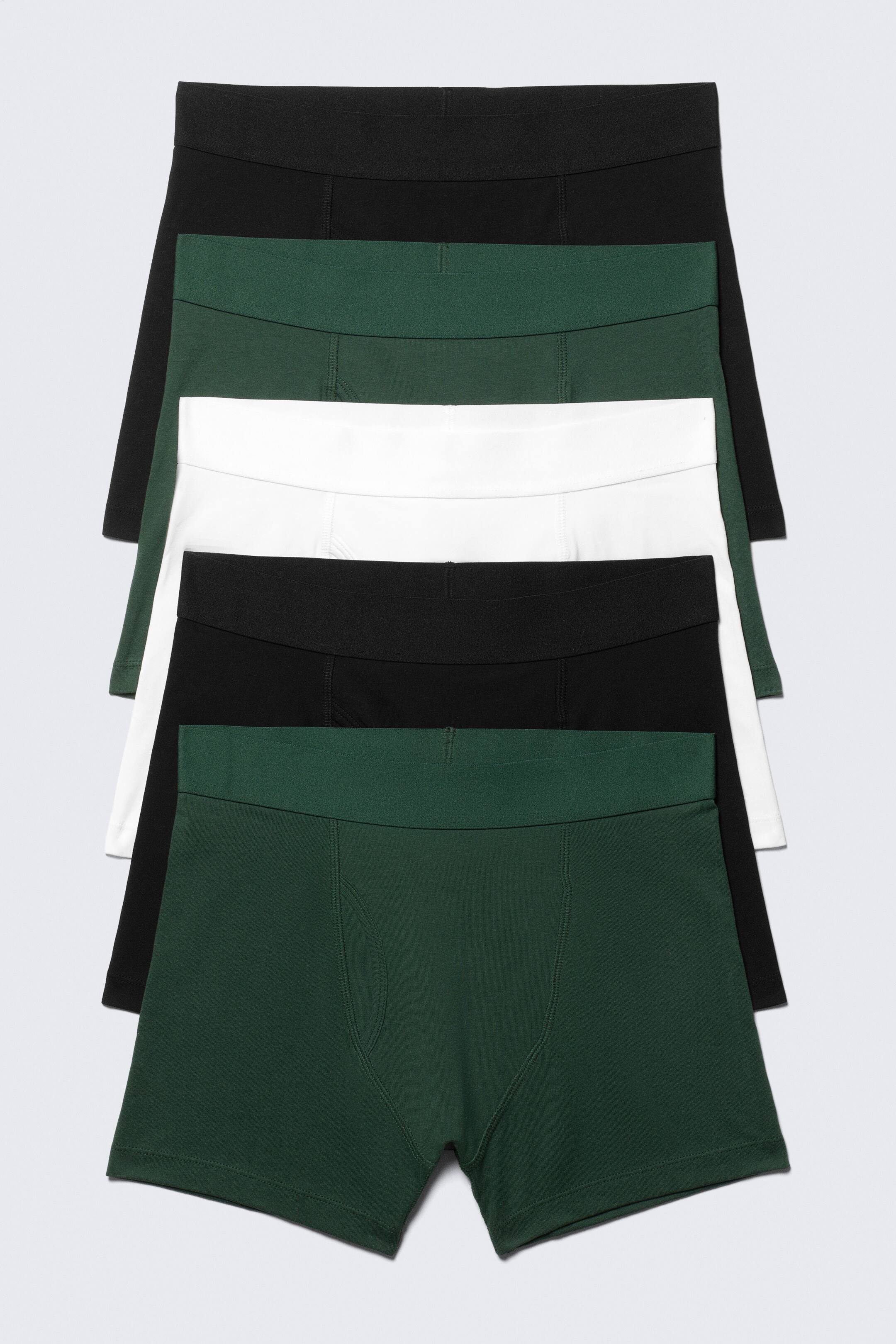 Visa större bild: Fem par herrboxerkalsonger visas framifrån, staplade och utspridda, med två svarta, två mörkgröna och ett vitt par. Varje par är designat med en monokrom elastisk midja och synliga sömmar som framhäver fickan.