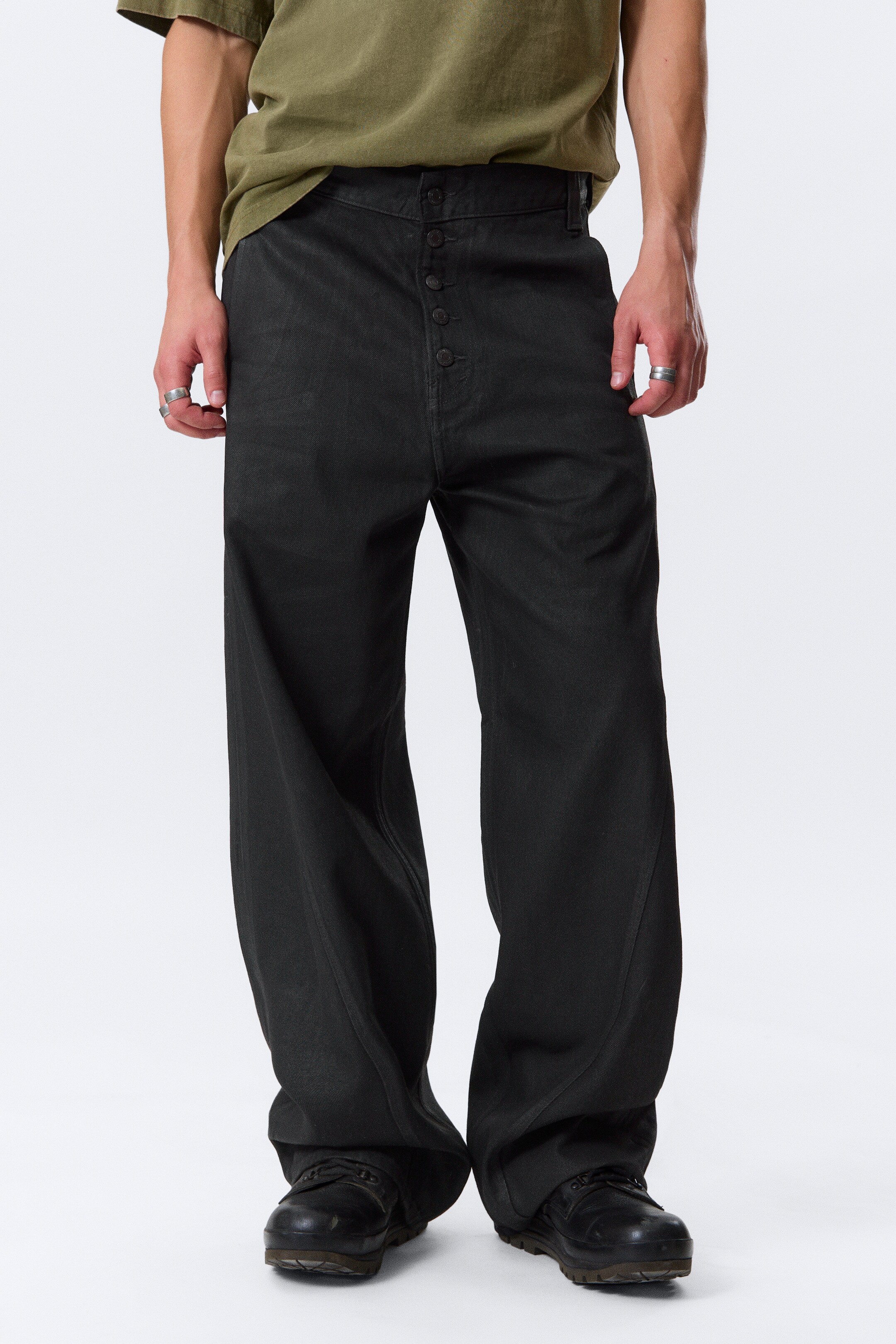 View larger image: Washed black, wide-leg pants are presented from a straight-on front view, featuring a high-rise waist with a prominent button fly closure displaying multiple buttons. The pants are showcasing a relaxed fit with distinct curved seams running down the outer legs, creating a full silhouette that is pooling at the ankles.
