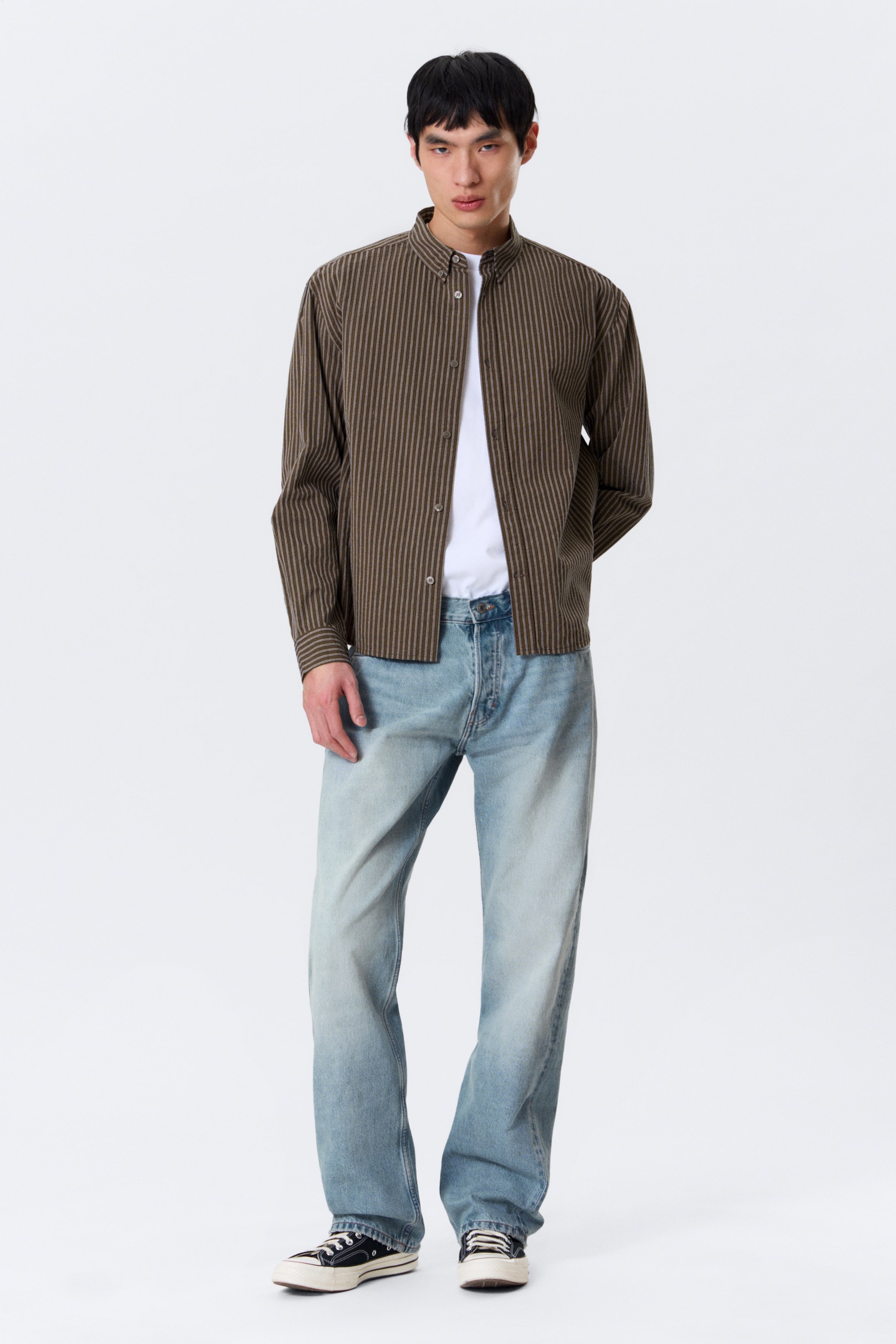 View larger image: The model is wearing a vertically striped relaxed-fit shirt featuring a band collar, front button fastening, and buttoned cuffs. The shirt is styled open over a white t-shirt.