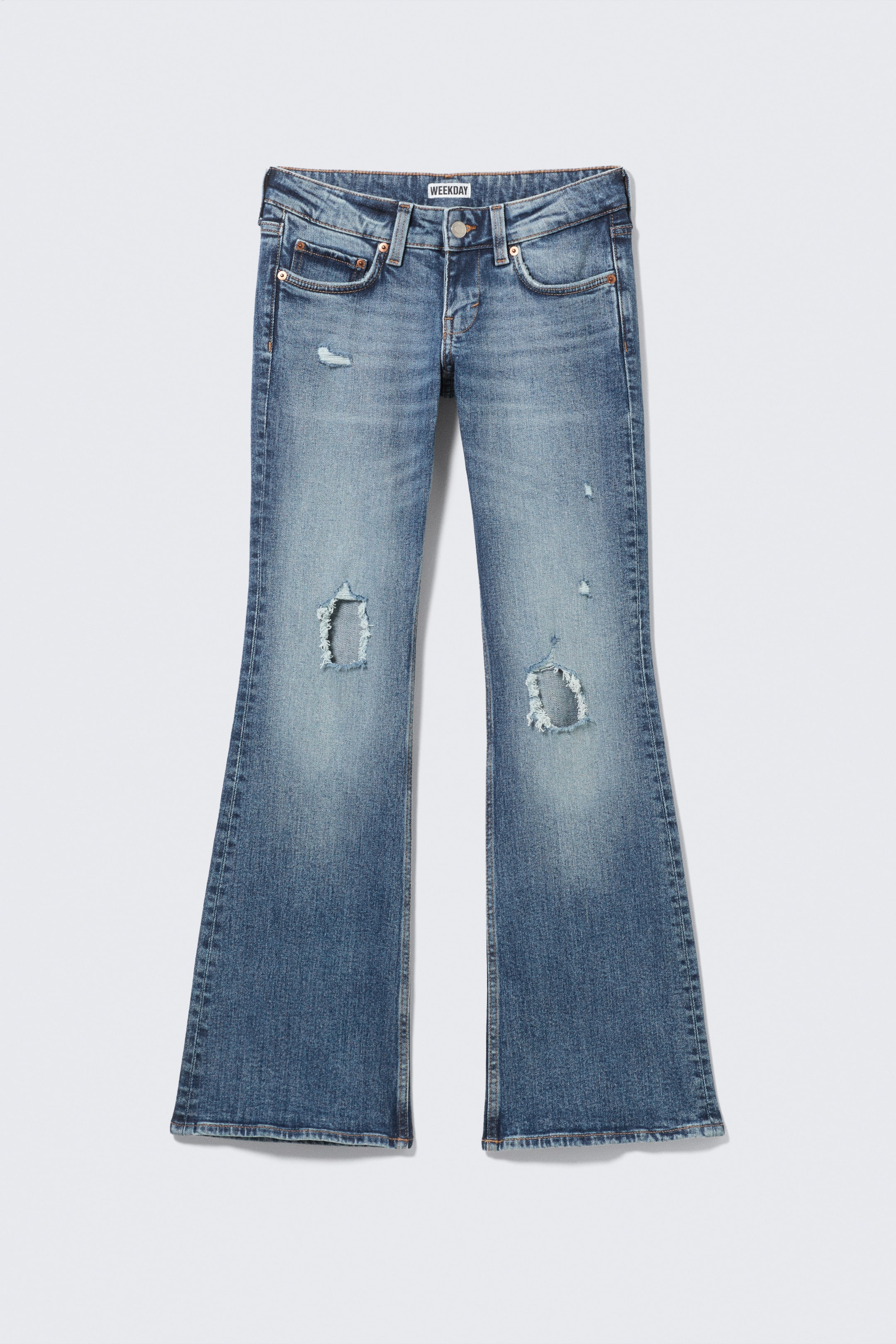 Agrandir l'image: Une paire de jeans flare en denim bleu, vue de face, présente un délavé, un whiskering au niveau des cuisses et des déchirures usées sur les deux genoux. Elle est dotée d'une coupe classique à cinq poches avec fermeture par bouton et braguette zippée, et une étiquette "WEEKDAY" est visible sur la ceinture.