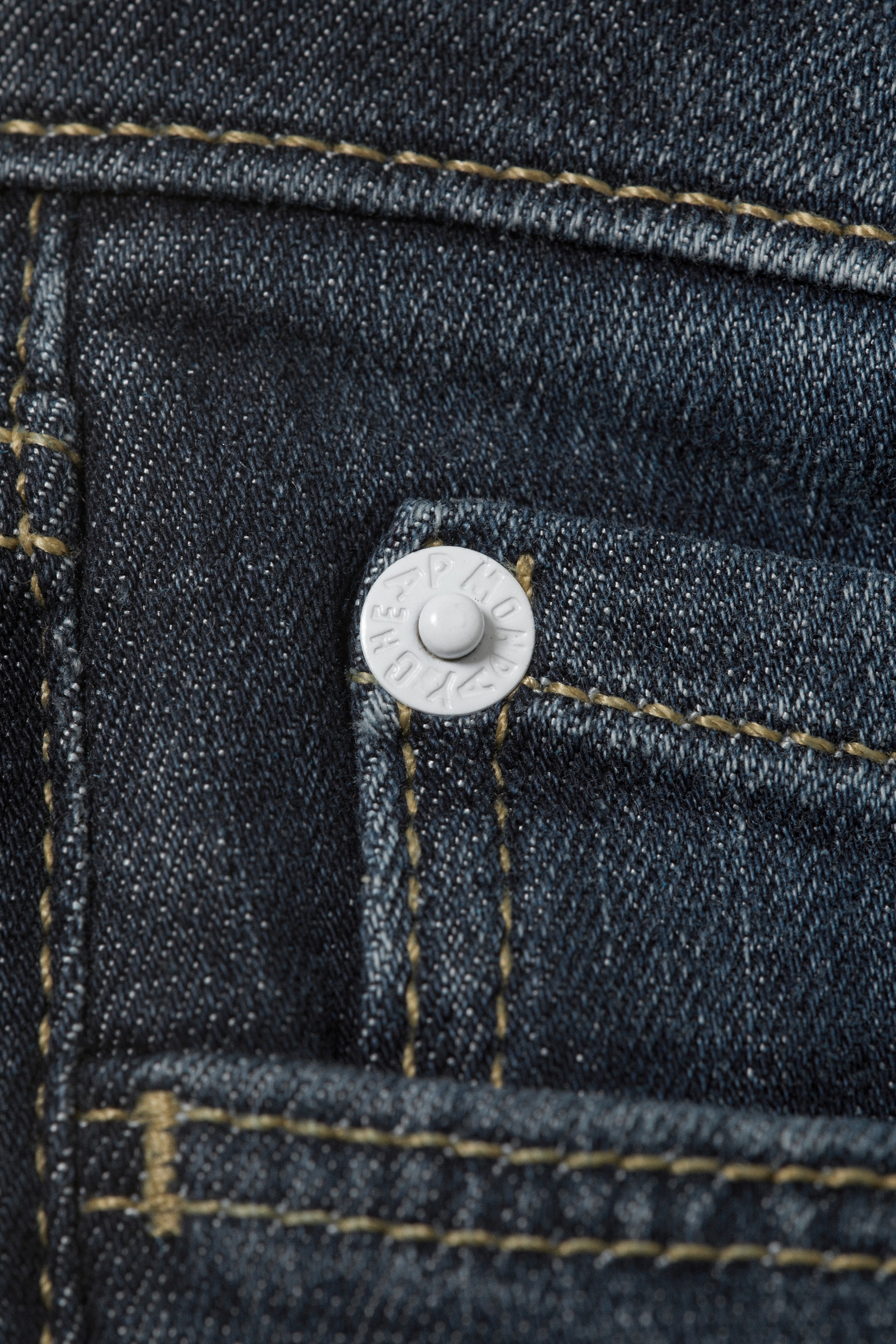 Visualizza immagine più grande: I jeans Booty Bei presentano un denim blu scuro con cuciture a contrasto marrone chiaro. Un bottone bianco è posizionato nell'angolo superiore di una piccola tasca anteriore.