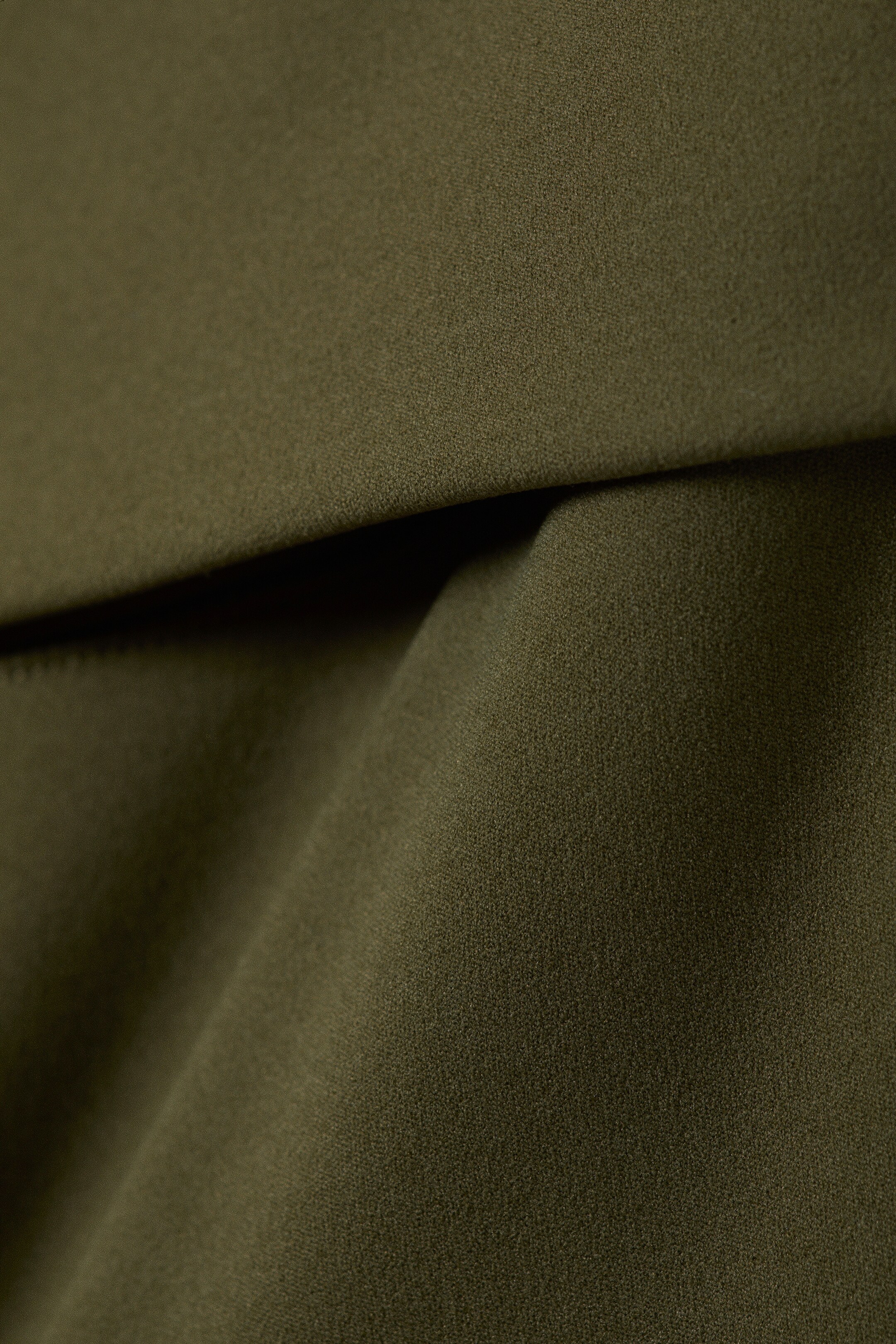 Agrandir l'image: Un tissu vert olive foncé à texture fine se plie et se drape doucement, mettant en valeur sa surface subtile et sa qualité souple.