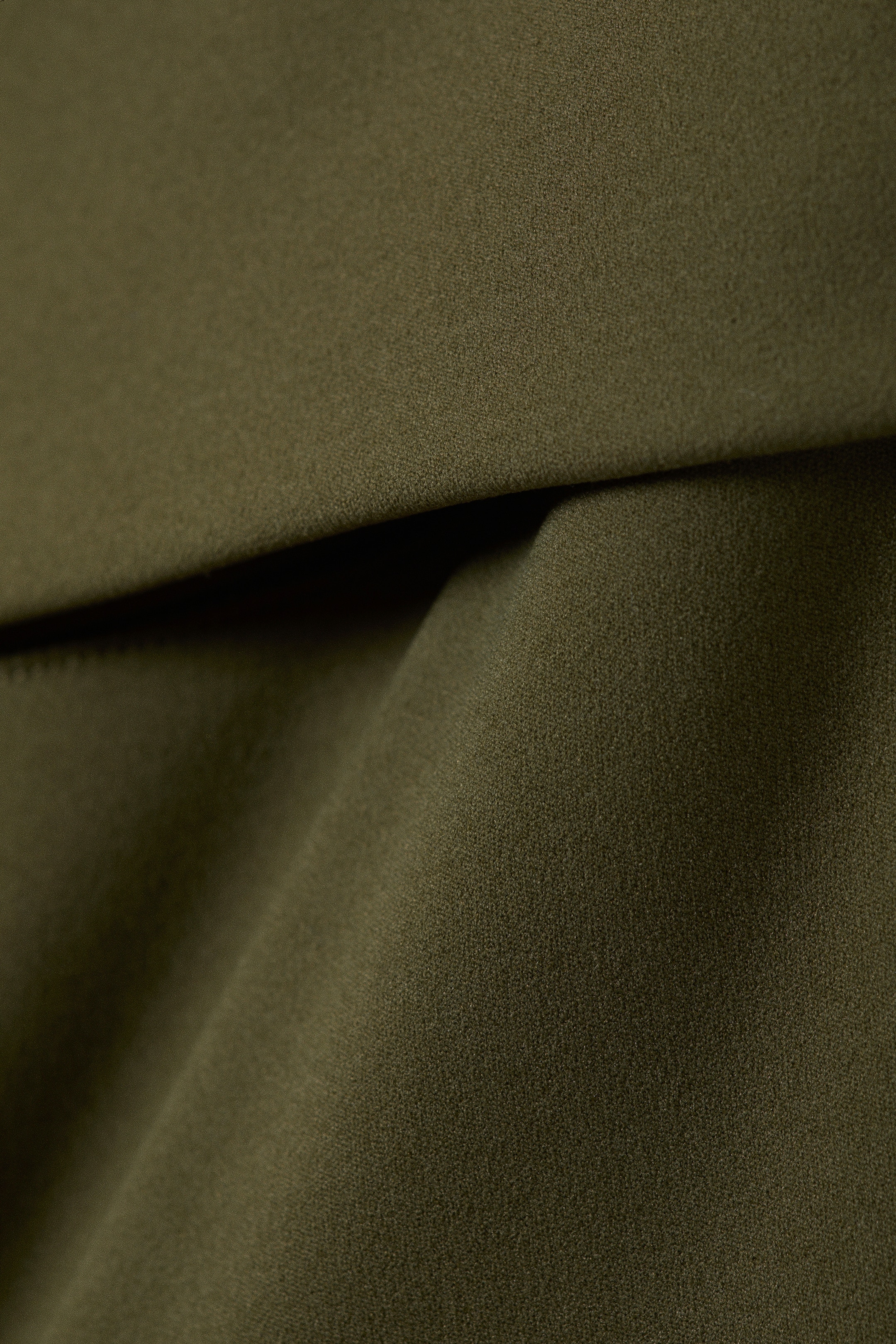 Ver imagen más grande: Una tela de color verde oliva oscuro finamente texturizada se pliega y cae suavemente, mostrando su superficie sutil y calidad flexible.