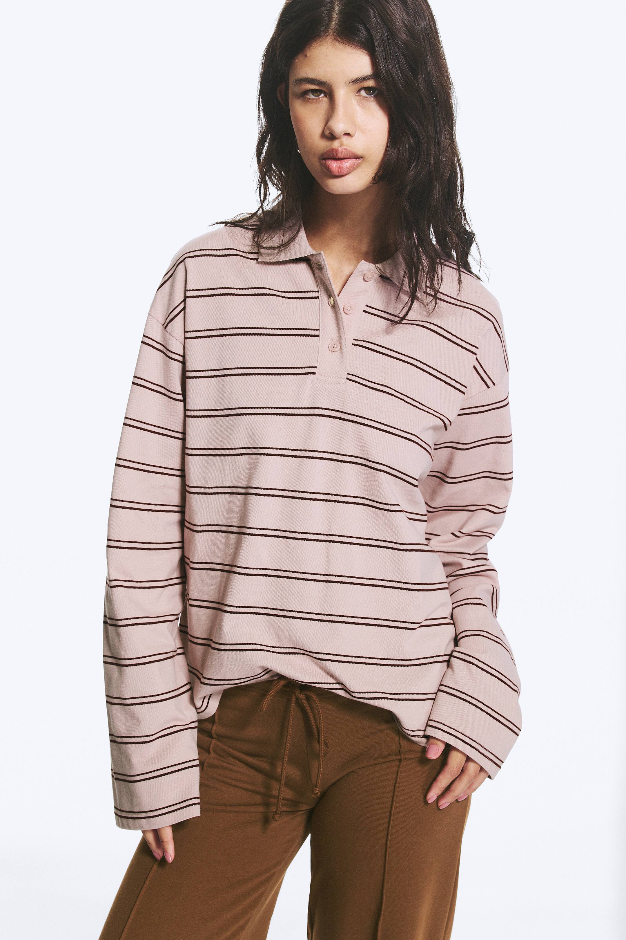 Größeres Bild ansehen: Ein langärmliges Poloshirt mit hellrosa Grundfarbe und dünnen, dunklen horizontalen Streifen, einem klassischen Polokragen, einer Drei-Knopf-Leiste und geraden Manschetten.