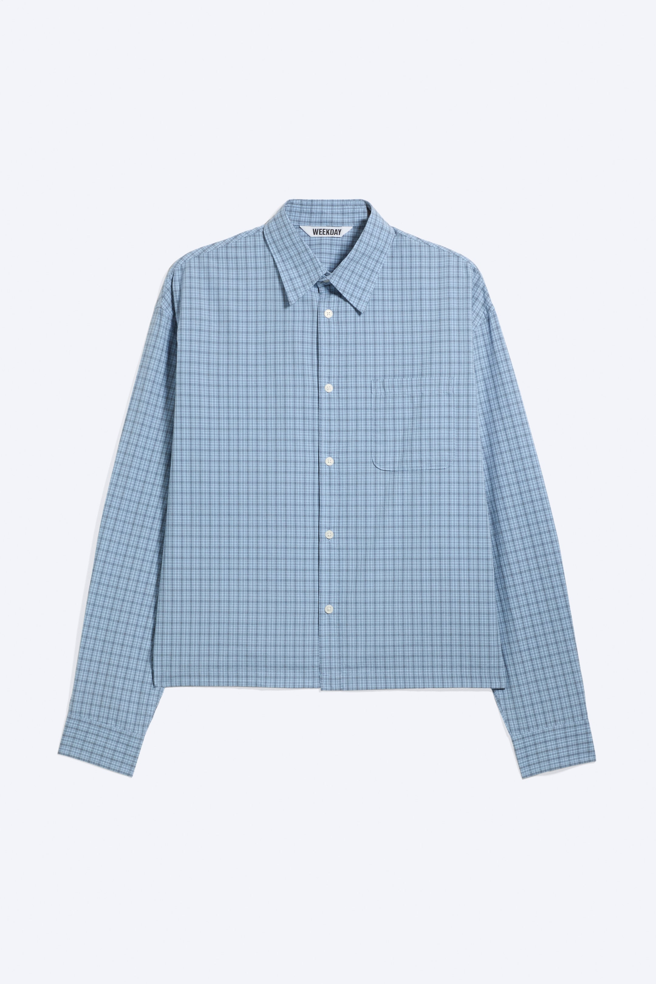 View larger image: A front view of a relaxed, boxy-fit shirt in a light blue check pattern, featuring a classic turn-down collar, a front button fastening, and a single chest pocket. The shirt has long sleeves with buttoned cuffs and a straight hem.