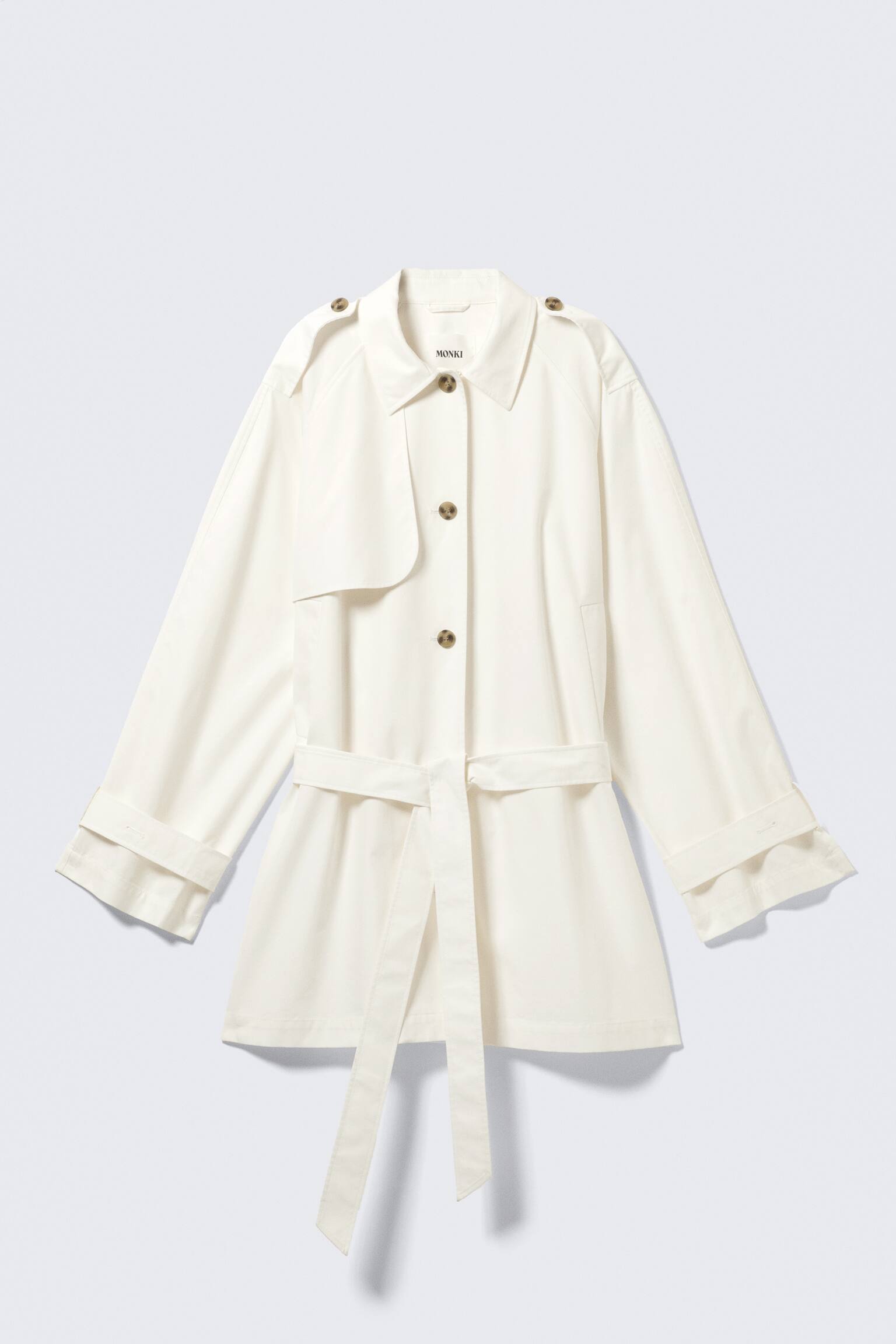 Un trench coat corto monopetto di colore bianco sporco è esposto dal DAVANTI, caratterizzato da una vestibilità ampia, un colletto a revers, spalline con bottoni e una patta per pistola sul petto sinistro. Una cintura a nastro stringe la vita, e le maniche lunghe terminano con polsini regolabili arrotolati.