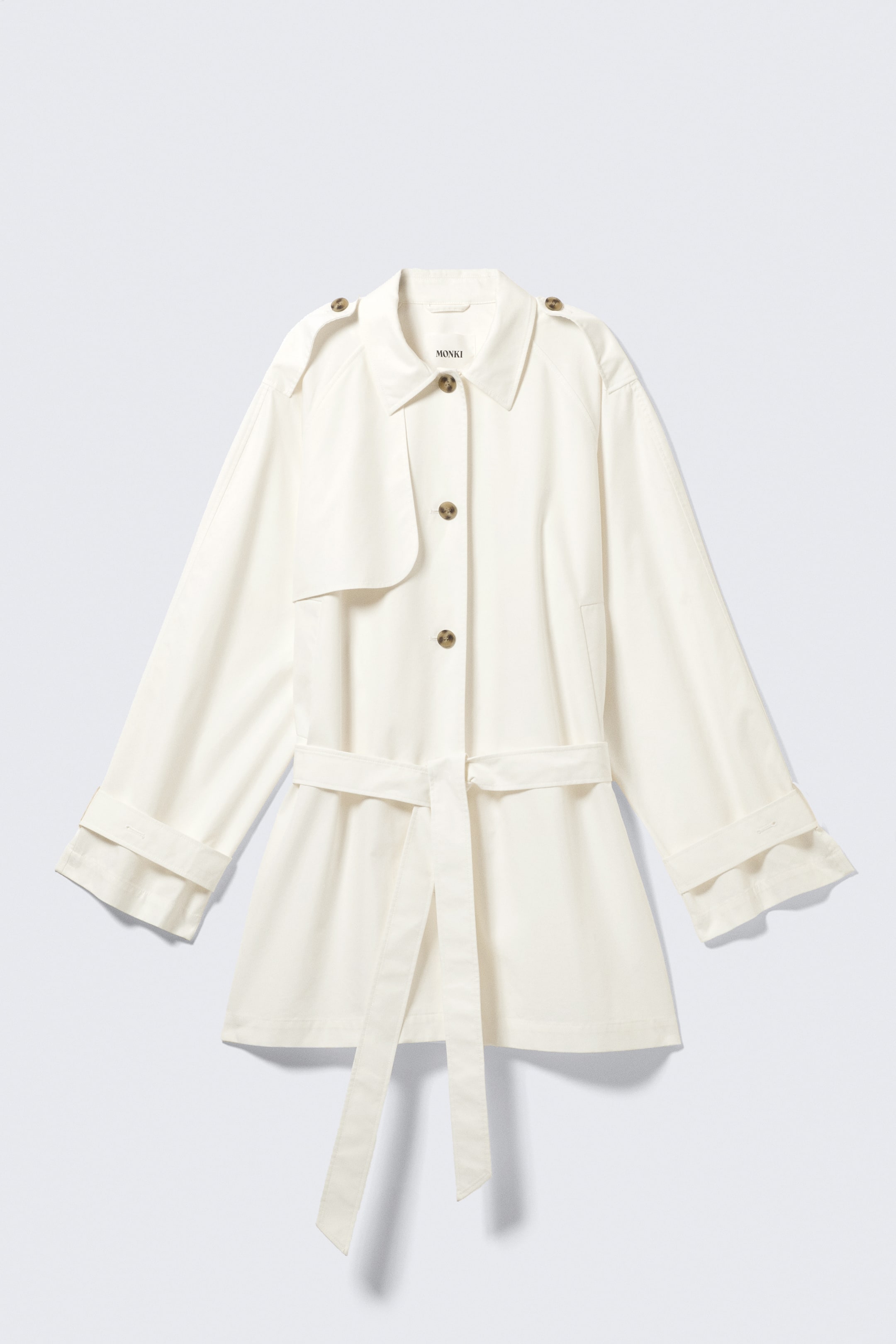 Größeres Bild ansehen: Ein kurzer, einreihiger Trenchcoat in einem cremeweißen Farbton wird von VORNE präsentiert. Er zeichnet sich durch eine lockere Passform, einen Umlegekragen, geknöpfte Epauletten und eine Sturmklappe auf der linken Brust aus. Ein Bindegürtel betont die Taille, und die langen Ärmel enden mit verstellbaren Manschetten, die hochgekrempelt sind.
