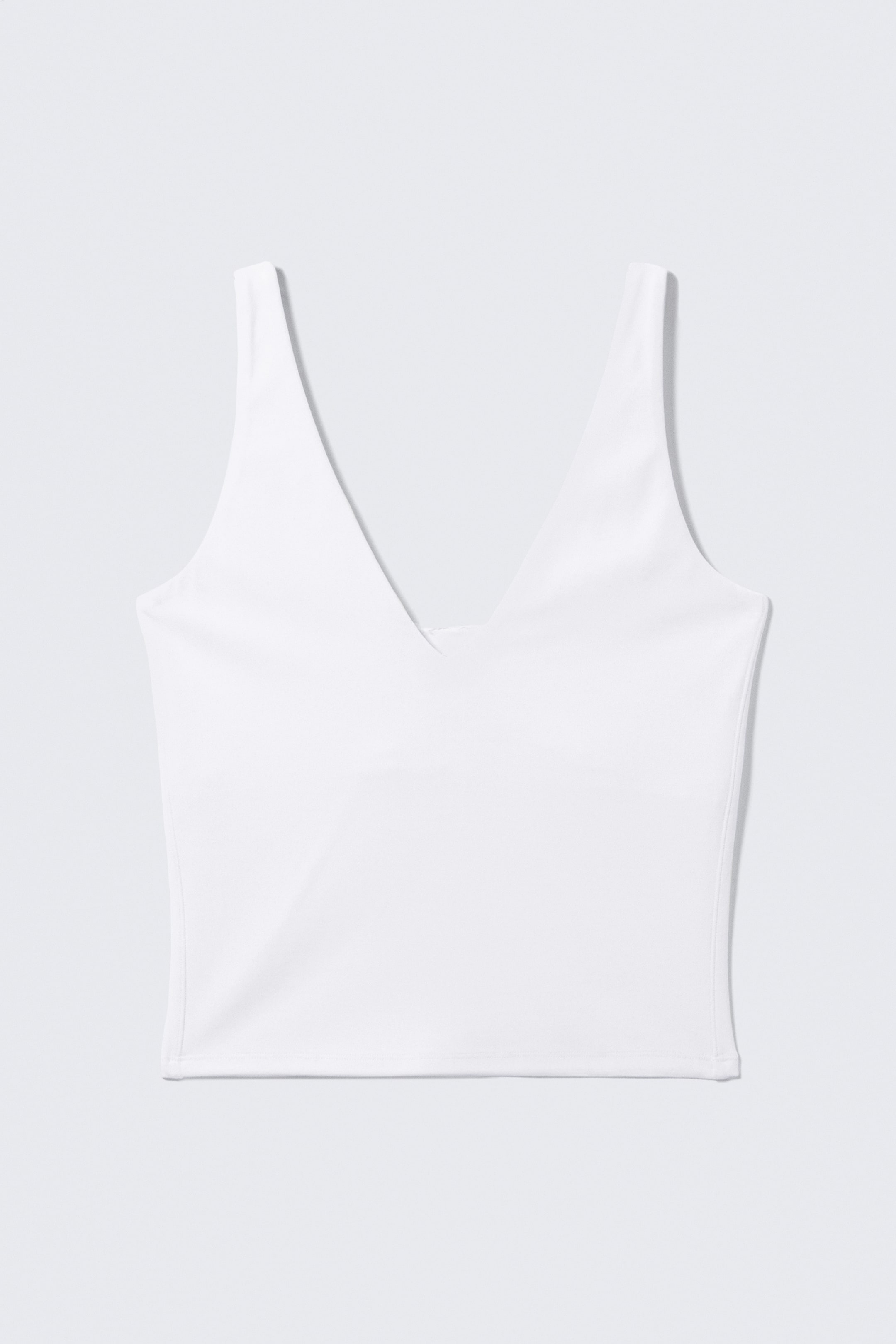View larger image: A white cropped sports top is facing forward, featuring a plunging V-neckline, wide shoulder straps, and a straight hem.