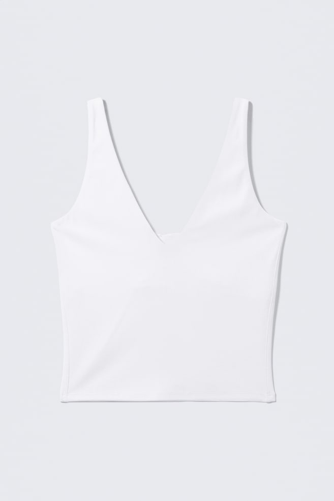 Un haut de sport blanc raccourci est orienté vers l'avant, avec un décolleté en V plongeant, de larges bretelles et un ourlet droit. - 1