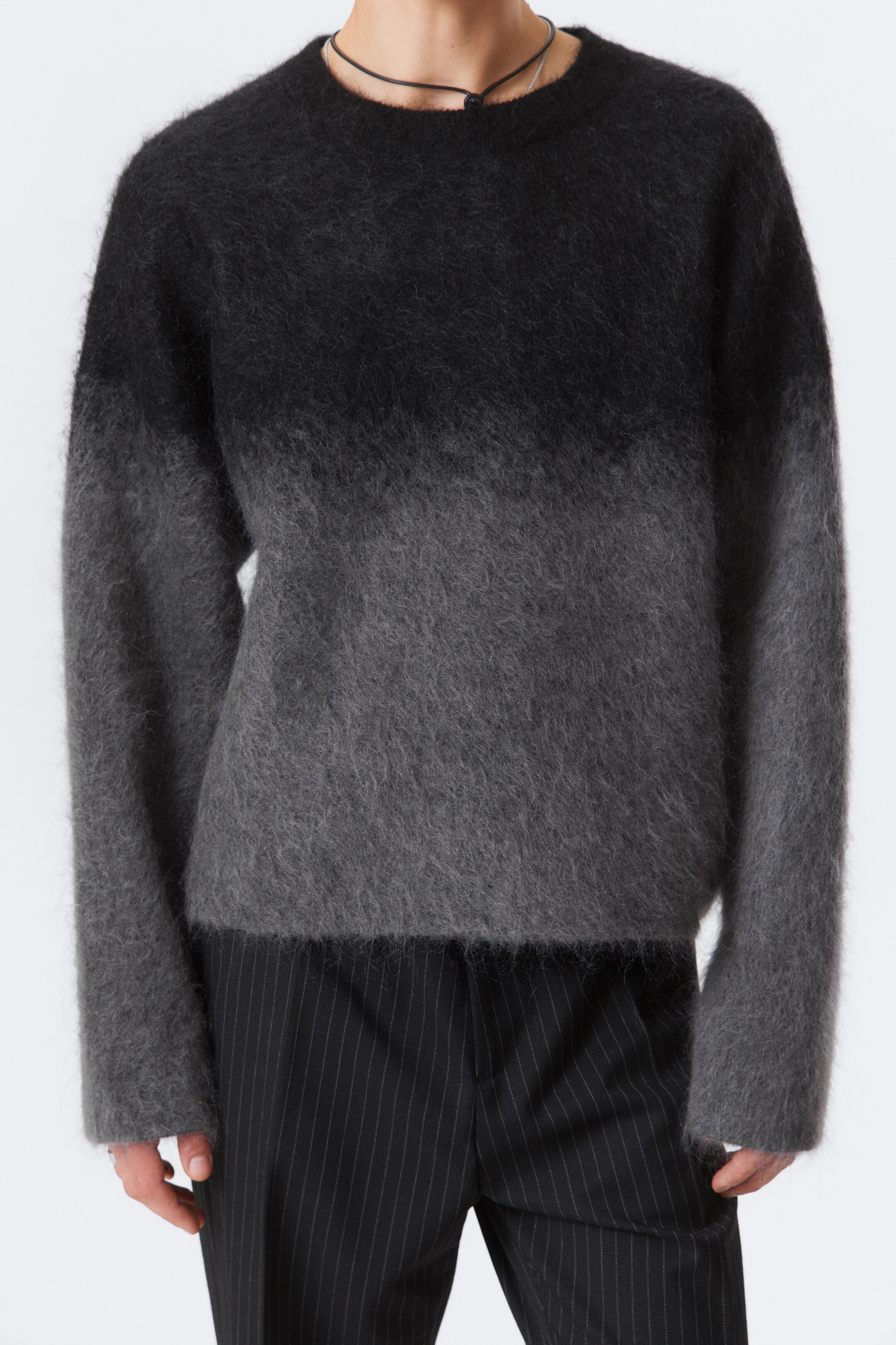 Visa större bild: En crewneck-tröja, med en lös passform och en borstad yta med en fluffig textur, bärs av modellen. Den visar en gradienteffekt från mörkgrå till ljusgrå, med raka kanter.