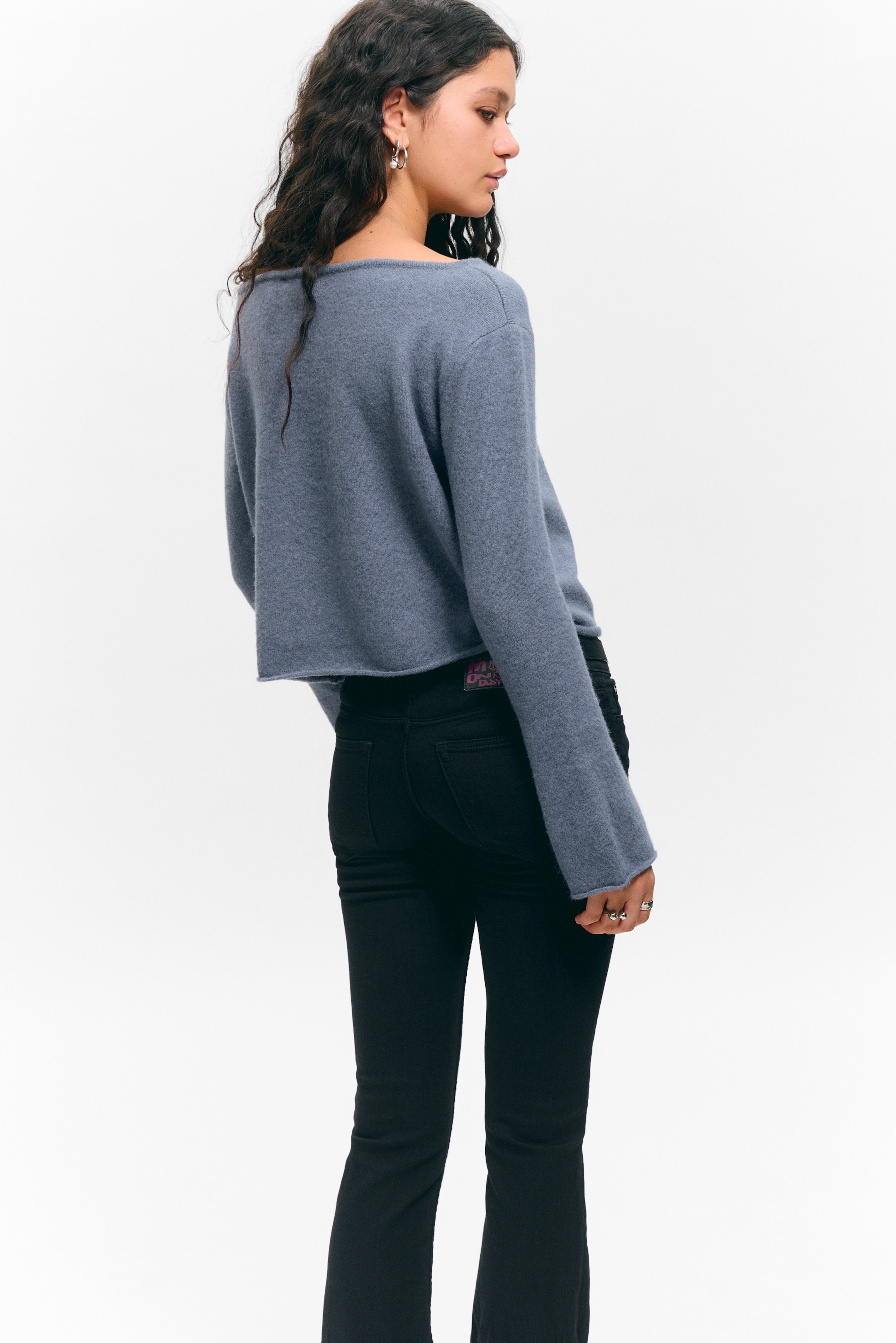 Größeres Bild ansehen: Ein blauer Pullover mit weicher Textur wird von hinten betrachtet und zeigt seinen breiten, rohkantigen Halsausschnitt und lange, lose Ärmel mit rohkantigen Bündchen. Der Pullover zeigt auch eine verkürzte Länge, die oberhalb der Taille endet.
