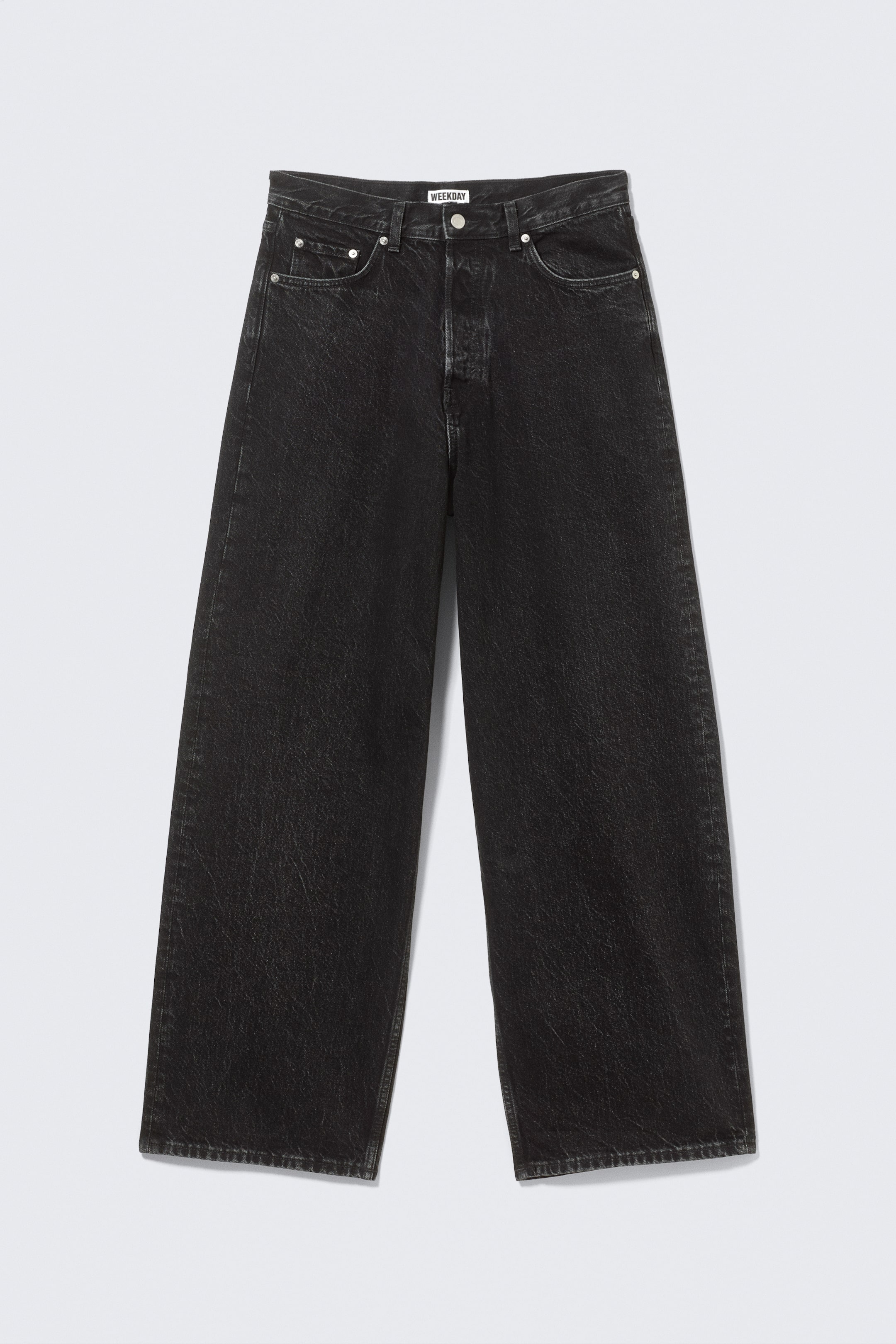 Agrandir l'image: Un pantalon large noir est montré de FACE, avec un délavage usé et une fermeture à boutons. Le design comprend cinq poches, des rivets argentés et une étiquette "WEEKDAY" sur la ceinture.