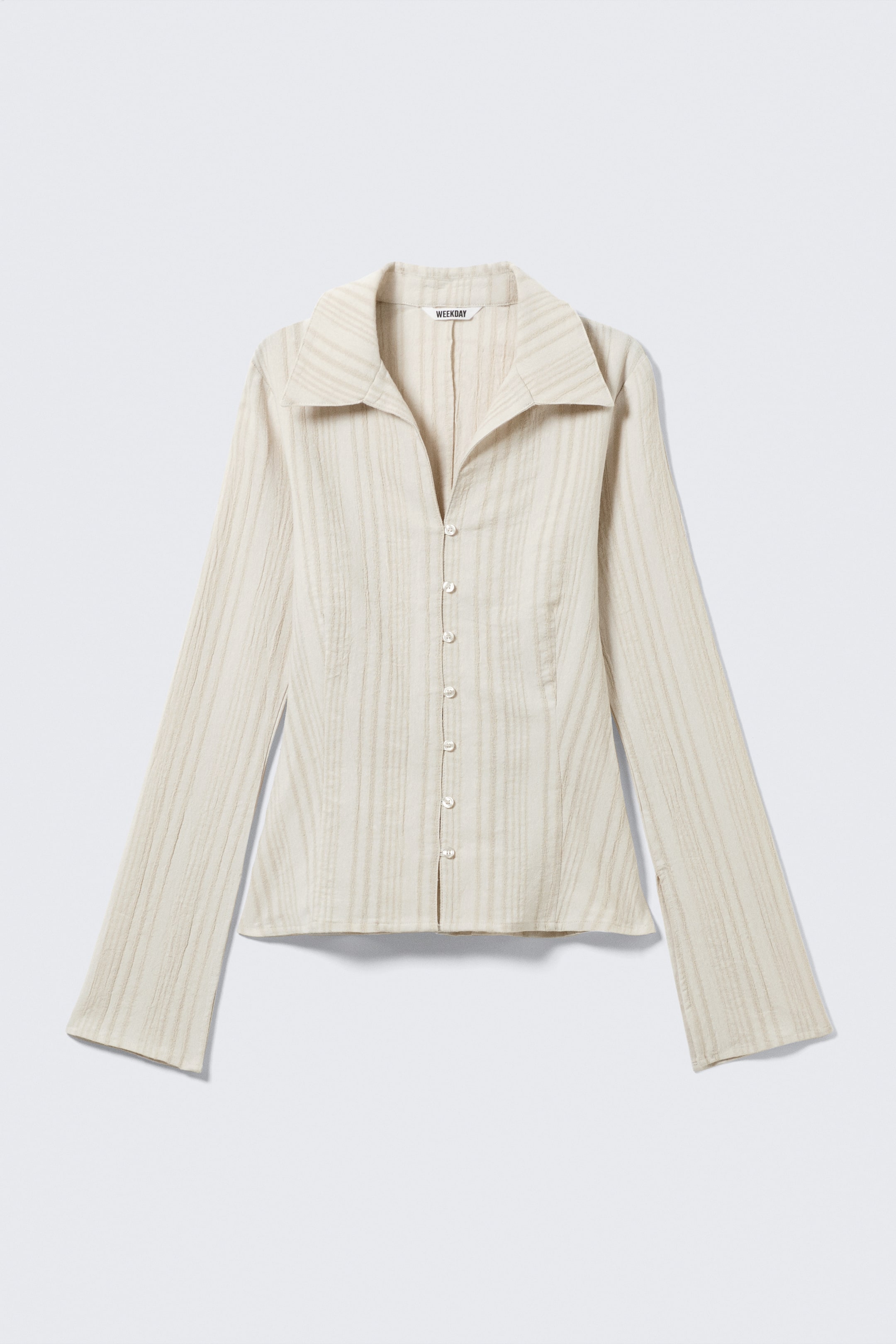 Größeres Bild ansehen: Eine hellbeige Bluse mit Knopfleiste wird VORNE präsentiert, die eine schmale Passform und eine strukturierte Oberfläche mit vertikalen Streifen aufweist. Sie ist mit einem V-Ausschnitt, langen ausgestellten Ärmeln und einem scharfen, gespreizten Kragen mit kantengestepptem Doppellagen-Design gestaltet, während kleine, hellfarbene Knöpfe die vordere Knopfleiste schließen.