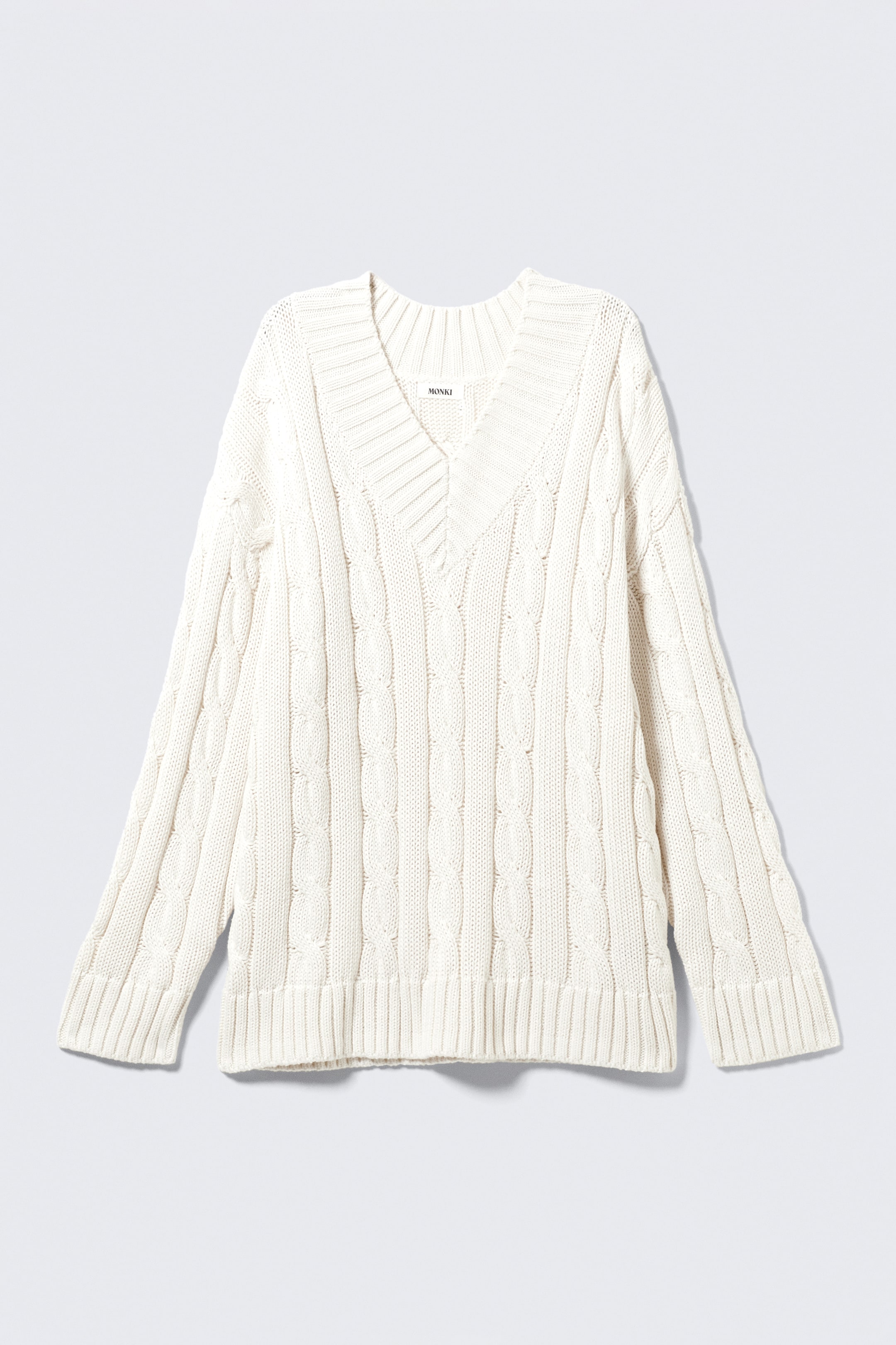 Agrandir l'image: Un pull crème à col en V présente son DEVANT, avec une silhouette oversize ornée d'un motif torsadé intégral et des bordures côtelées larges au niveau du col, des poignets et de l'ourlet.