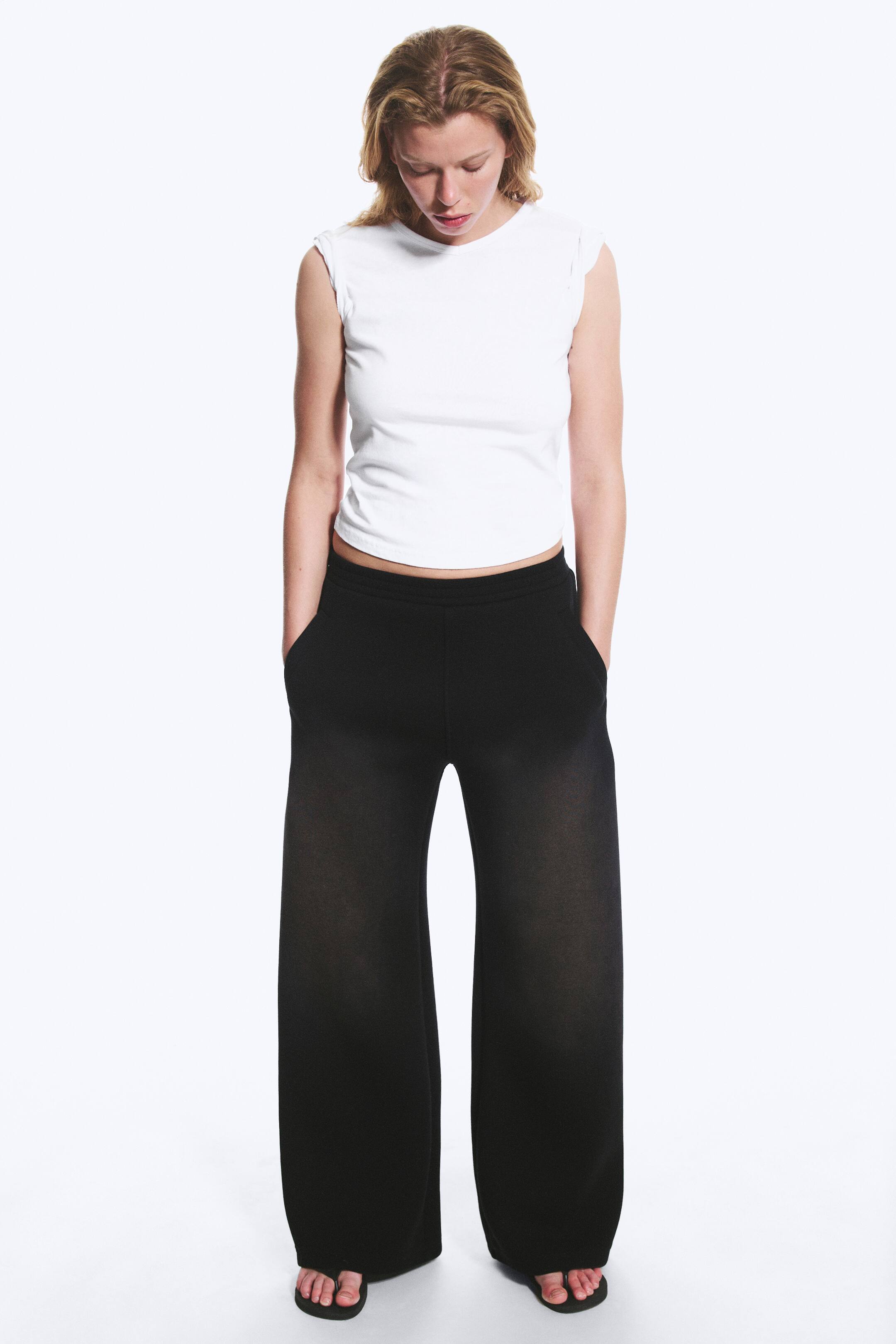 Agrandir l'image: Pantalon noir à jambes larges présentant une coupe palazzo pleine longueur, avec une taille élastiquée et des poches latérales. Les mains reposent dans les poches, mettant en valeur leur emplacement et la silhouette décontractée et fluide du pantalon.
