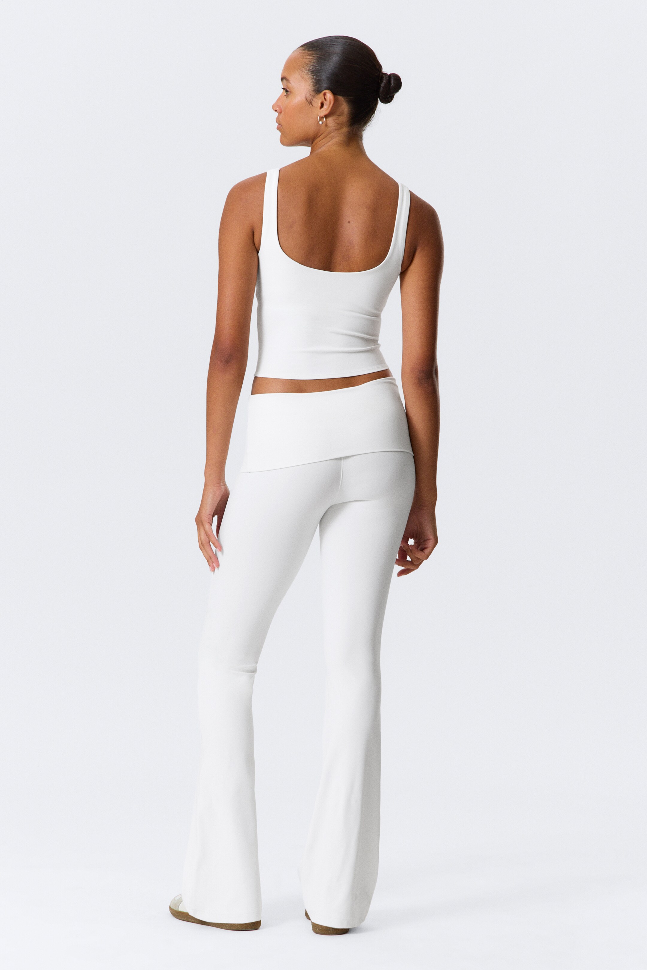 Agrandir l'image: Un débardeur blanc raccourci est montré de dos, avec un décolleté en U et de larges bretelles. Un pantalon blanc taille haute est également présenté, ajusté au niveau des hanches et des cuisses, avec une large ceinture repliée et une silhouette évasée à partir du genou.