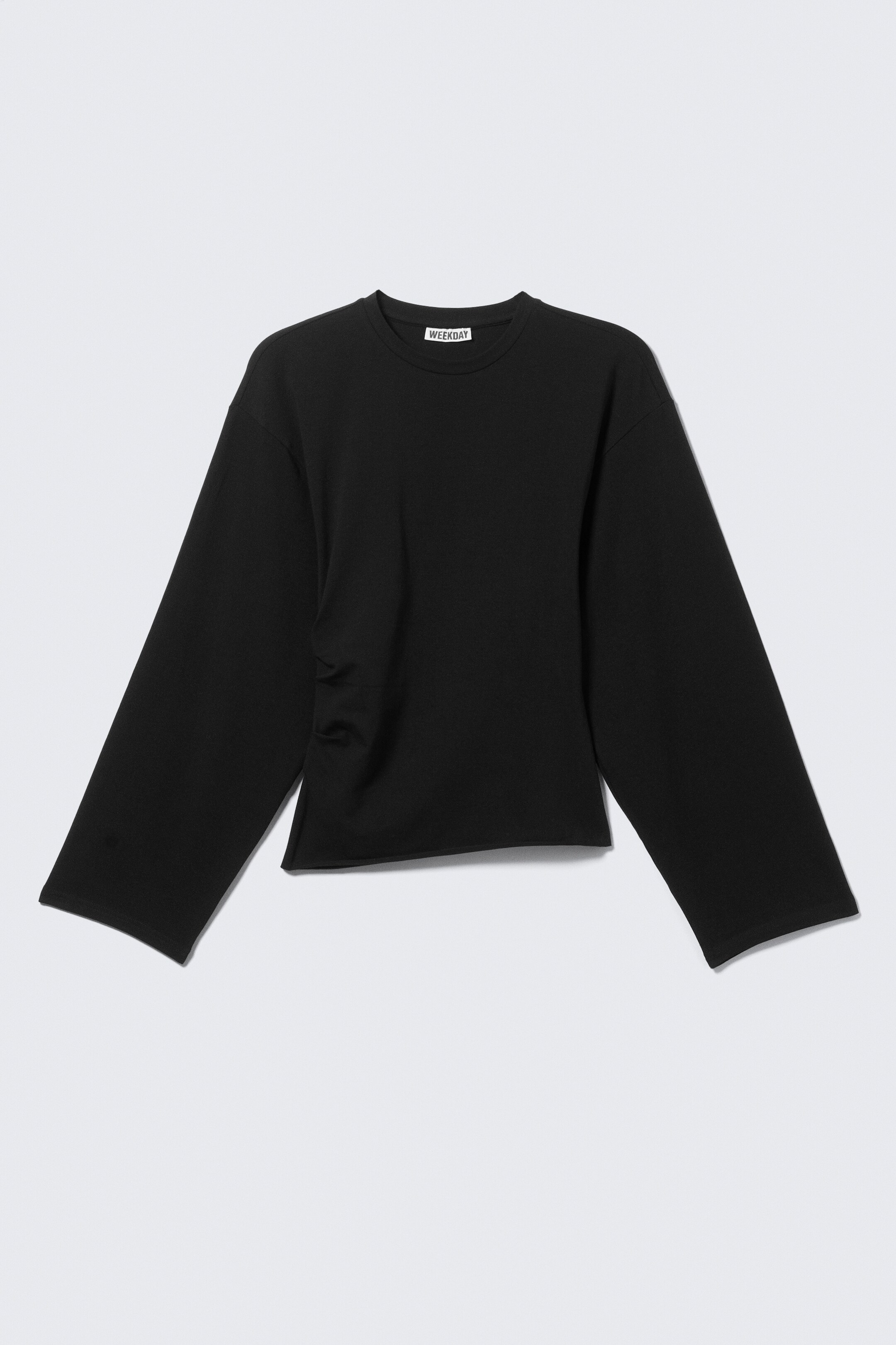 Visa större bild: En svart långärmad topp presenteras FRAM, med en rund hals och breda, avslappnade ärmar. En rynkdetalj syns på dess vänstra sida.