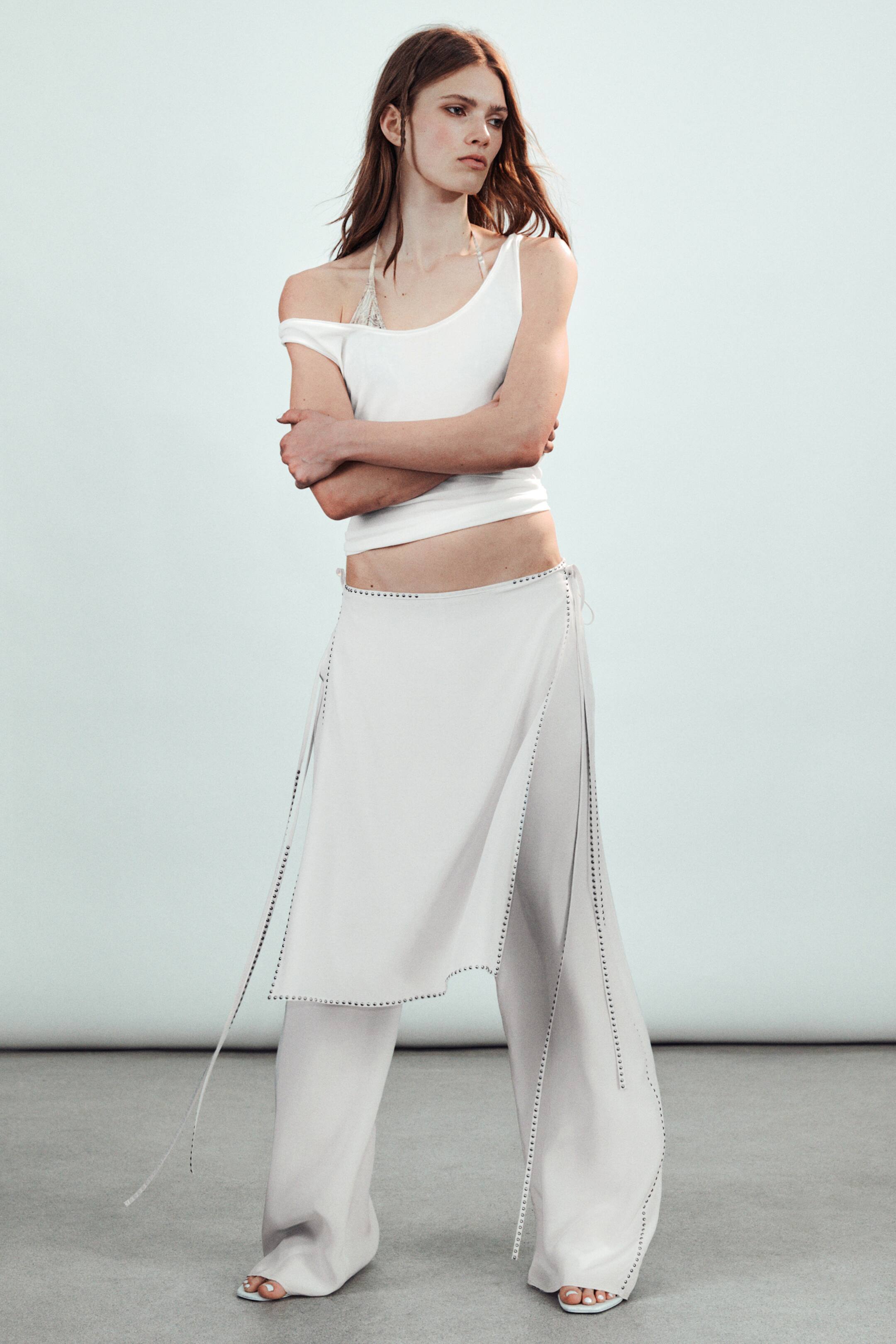 View larger image: The model is wearing a mid-rise skort, crafted with a fluid drape, featuring an overlapping tie skirt layered over loose-fitting trousers. This creates a relaxed, wrapped silhouette with stud detailing along the seams.