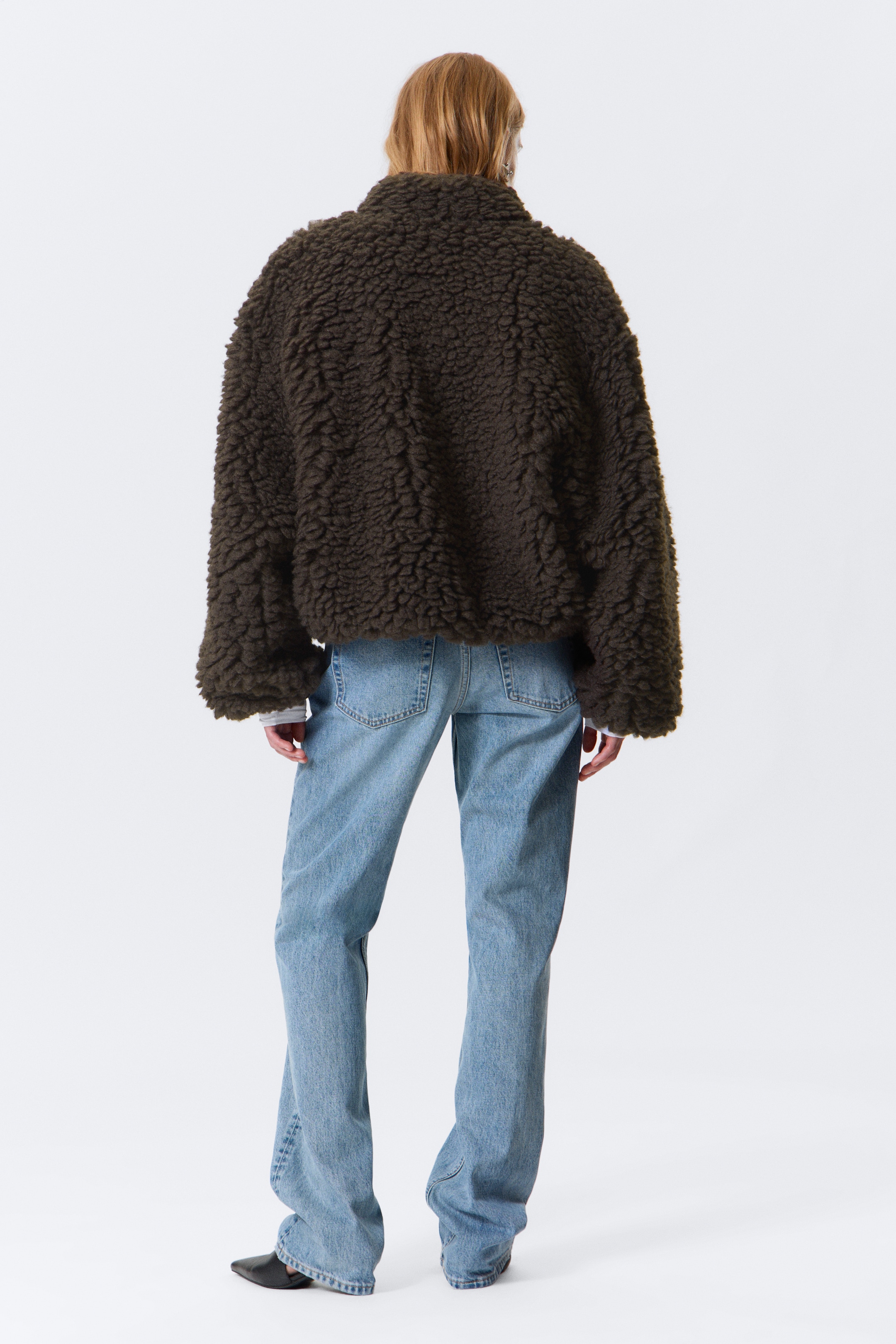 Ver imagen más grande: Una chaqueta de color verde oscuro y textura peluda se está usando, vista desde atrás. La chaqueta presenta un cuello alto y mangas anchas de largo completo, y está recortada a la cintura, revelando unos jeans azul claro y los puños de una camiseta de manga larga de color más claro debajo.