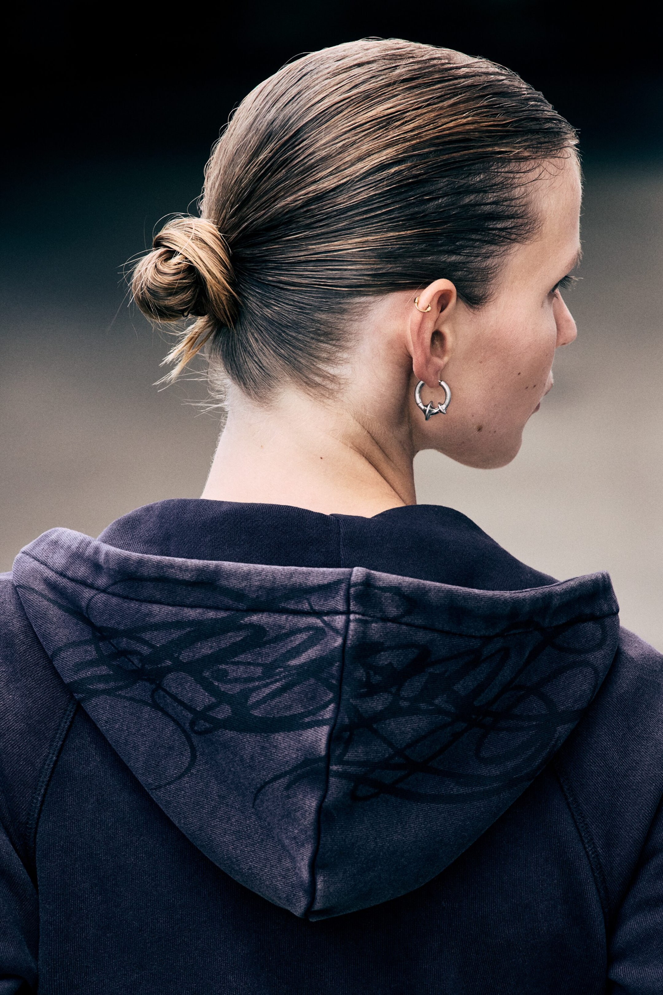 View larger image: A slim-fit hoodie in a faded dark purple wash is being worn by the model, viewed from behind. The lowered hood features a black abstract scribble graphic printed across the fabric.