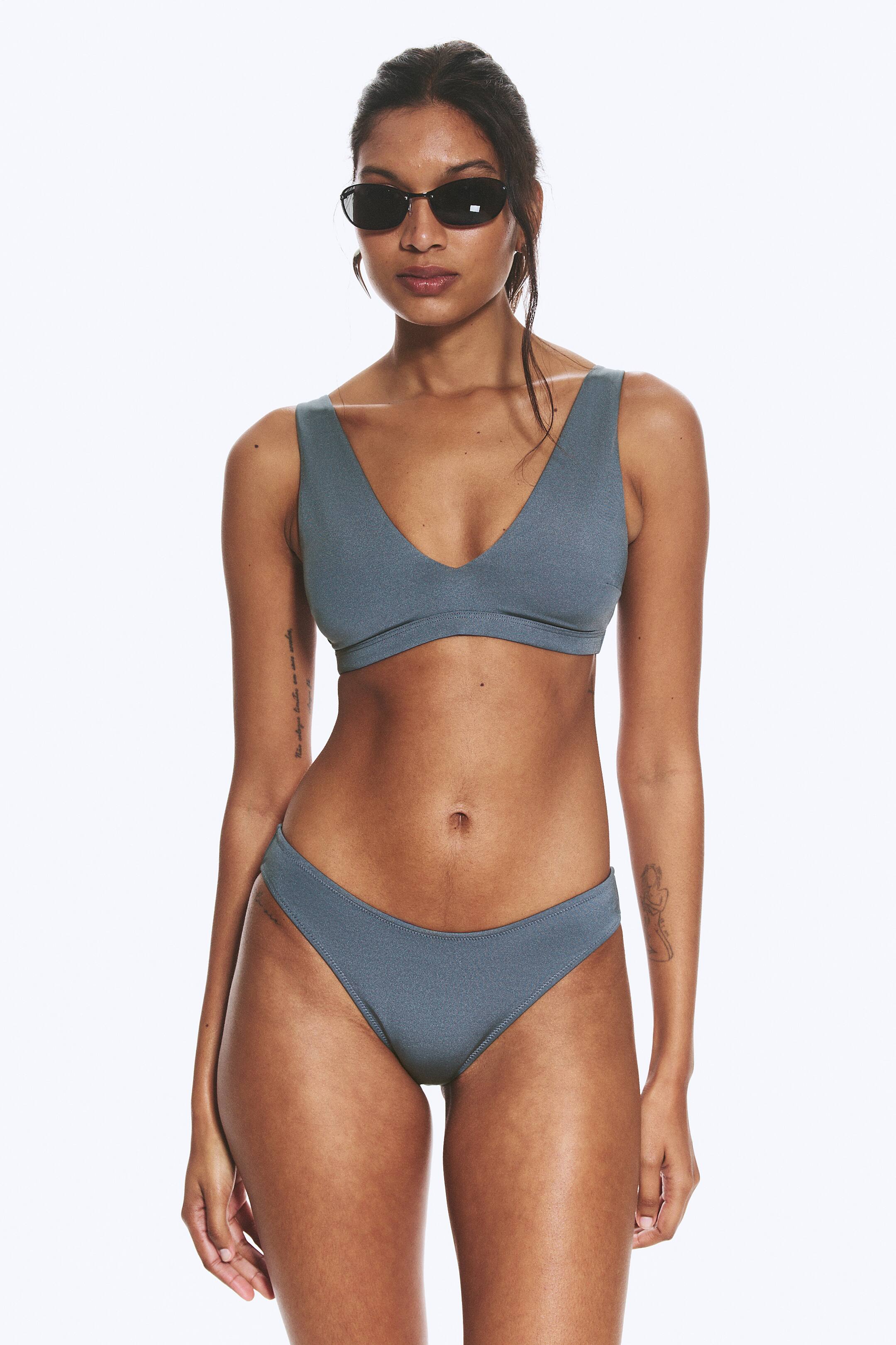 Ver imagem maior: É apresentado um fato de banho cinza ardósia de duas peças, com um top que apresenta um decote em V profundo, alças largas e uma faixa larga sob o busto. A parte de baixo do biquíni, de corte alto, exibe costuras visíveis ao longo das suas bordas.