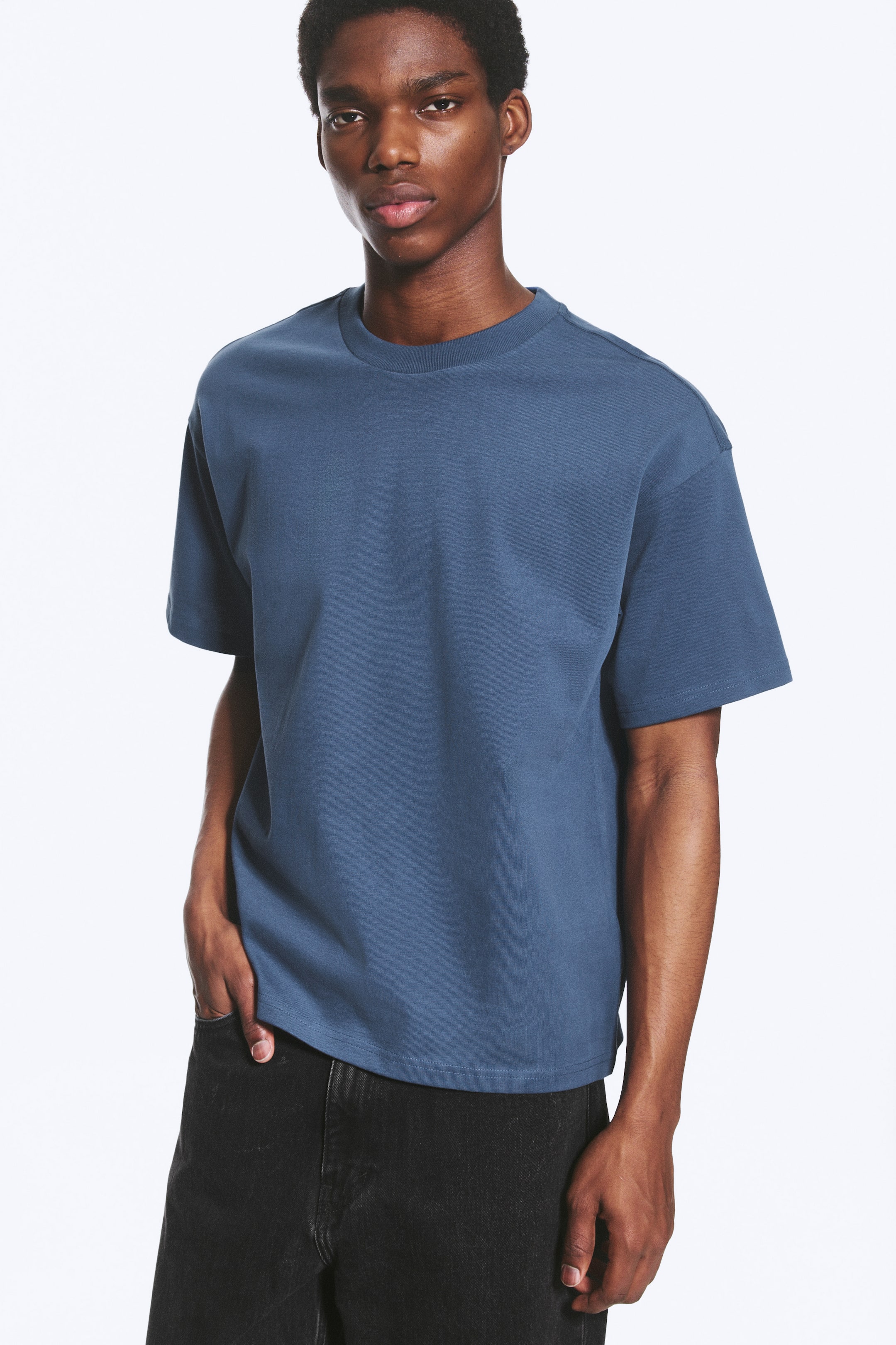 Grotere afbeelding bekijken: Een gedempte blauwe t-shirt met een ronde hals en korte mouwen met verlaagde schouders. Het heeft een ontspannen pasvorm en is naar voren gericht.