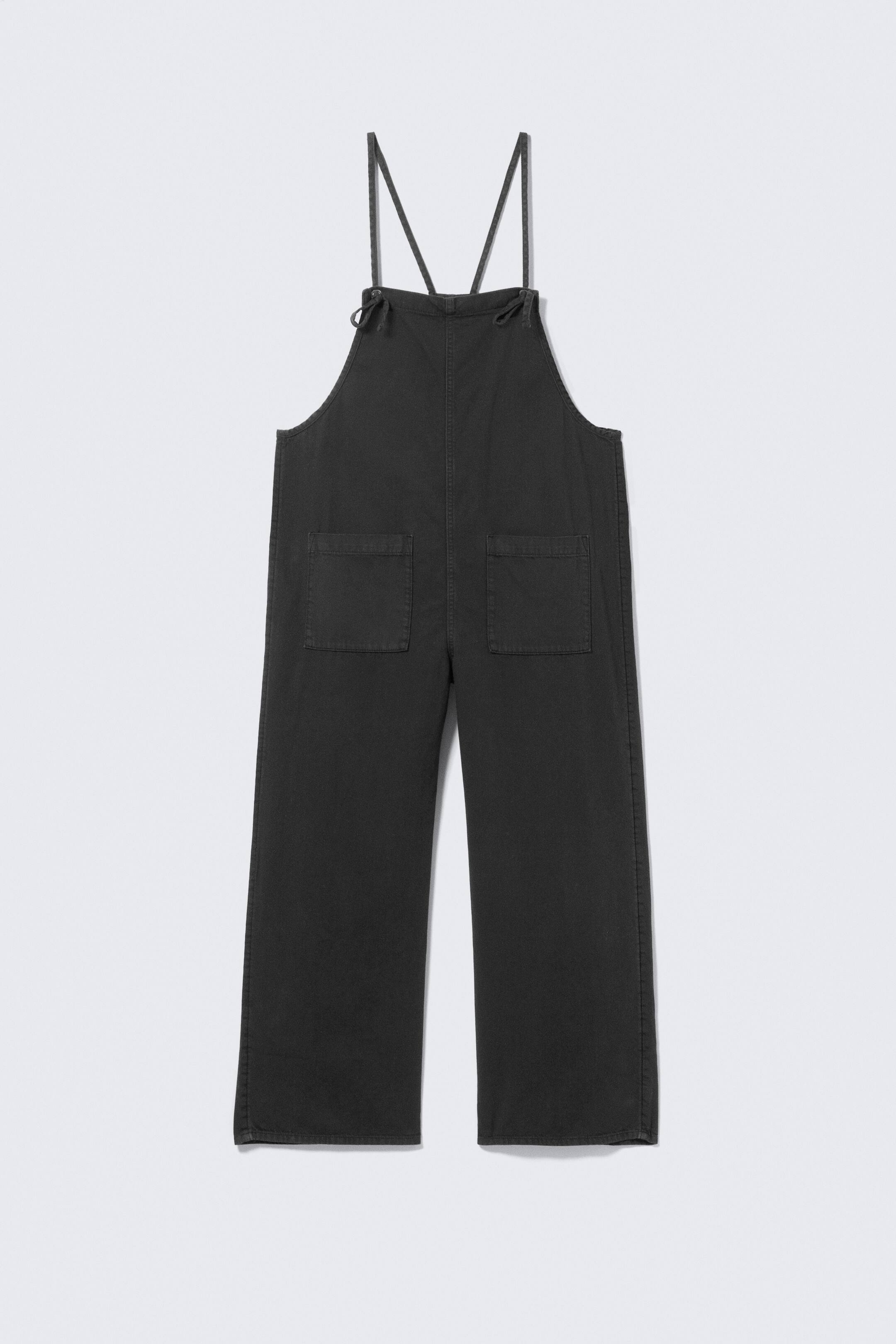 Ver imagem maior: Os macacões cinza escuro estão apresentados numa vista frontal, com um peitilho e alças finas que se atam nos ombros. Dois grandes bolsos retangulares tipo patch são visíveis no peitilho, e os macacões têm pernas largas.