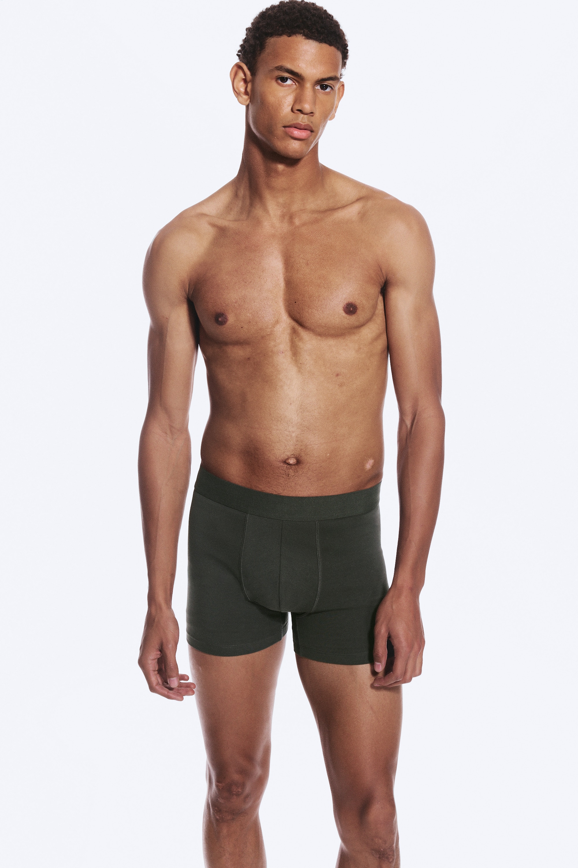Fünf Paar Boxershorts sind ordentlich in abwechselnden Schwarz- und Olivgrün-Tönen gestapelt, wobei jedes Paar über einen elastischen Bund und ein konturiertes Vorderteil verfügt.