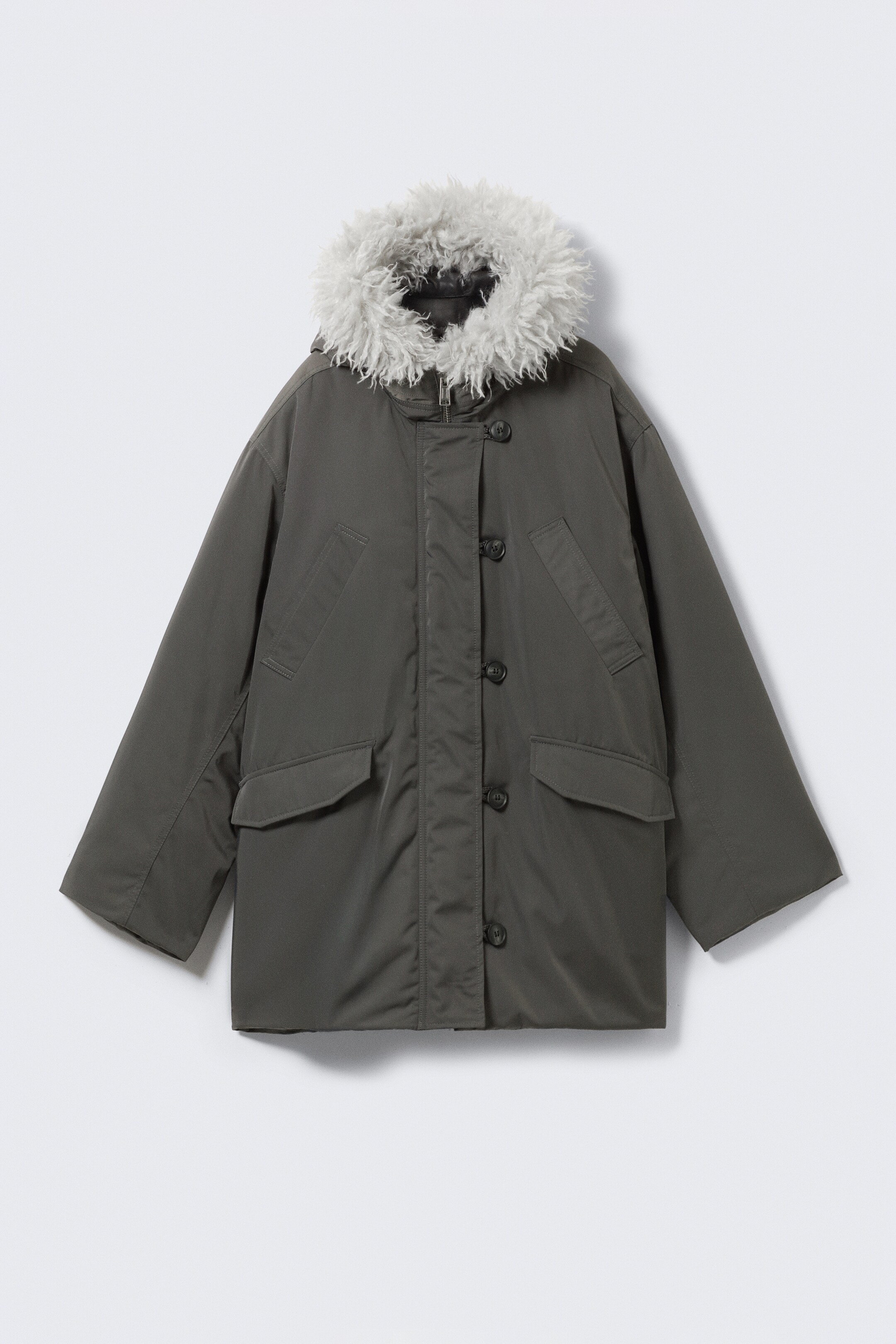 Grotere afbeelding bekijken: Een donkergroene parka wordt van de VOORKANT getoond, met een ontspannen pasvorm en een langwerpige silhouet. Het toont een dubbel gelaagde capuchon met een lichtgrijze, ruige faux fur rand, een centrale knoopsluiting die een verborgen ritssluiting bedekt, twee schuine borstzakken met paspel en twee lagere klepzakken.