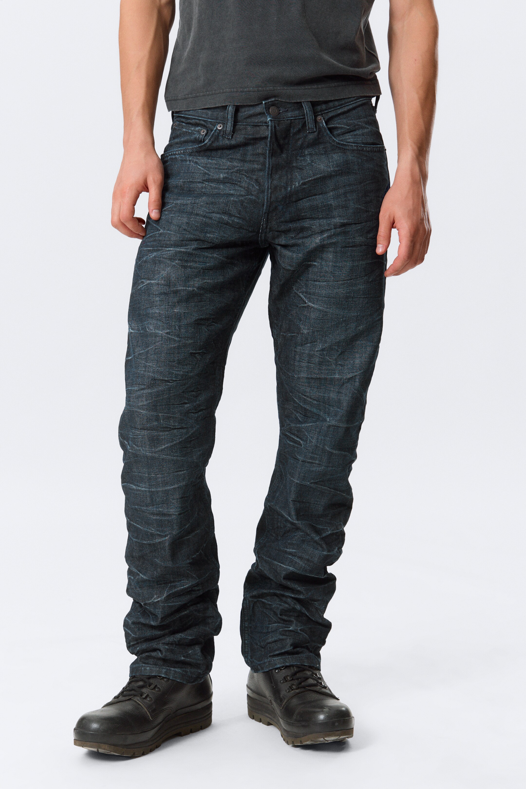 Se større billede: Forfra vises mørkvaskede denimjeans, der har en kraftigt krøllet tekstur med lysere highlights. Jeansene har en knaplukning, forlommer med scoop og en møntlomme, med en lige benpasform, der stakker kraftigt ved anklerne.
