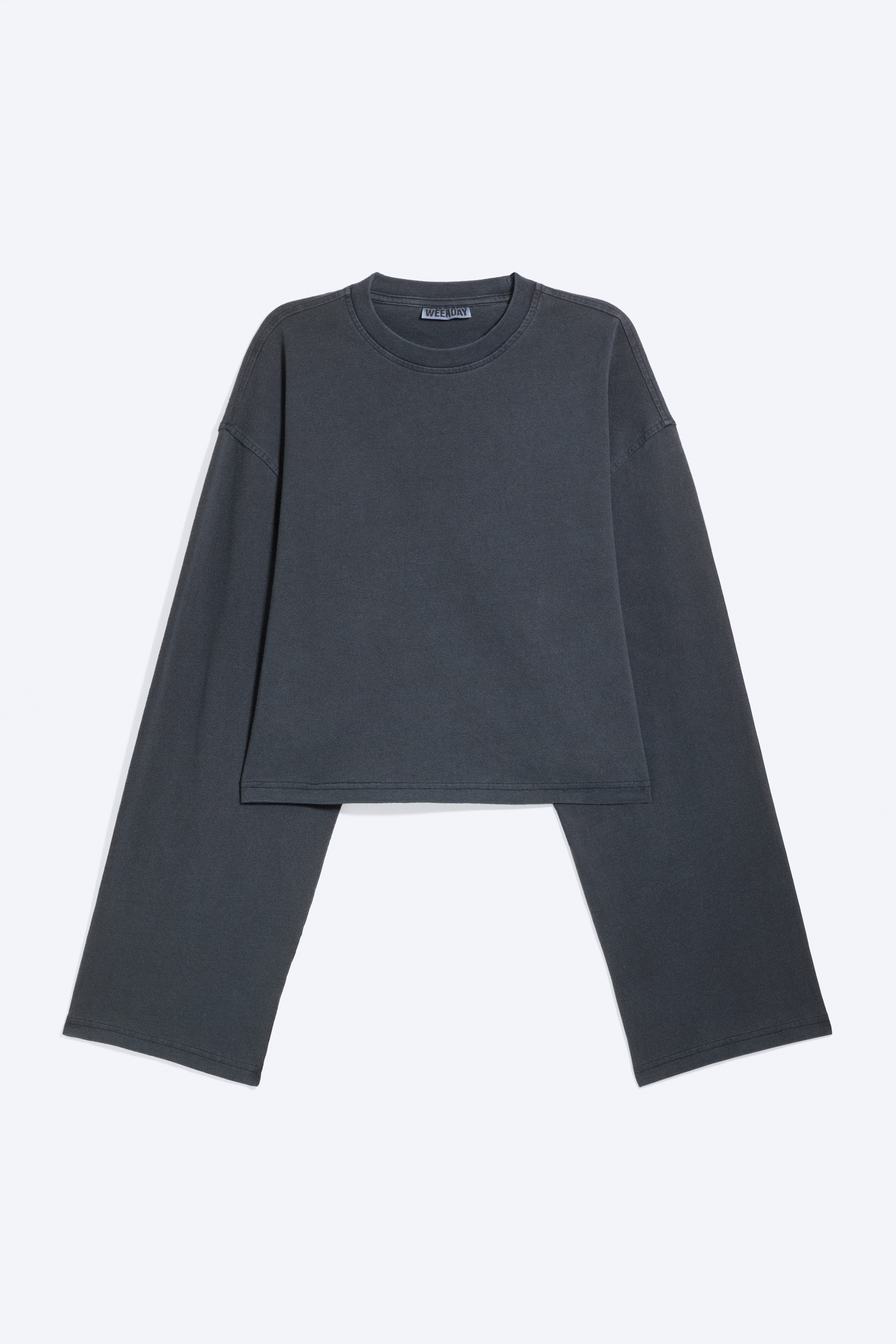 Le mannequin porte un T-shirt court Ã  manches longues, gris foncÃ©, avec un col rond et des Ã©paules tombantes. Ce haut ample et carrÃ© est superposÃ© sur une couche blanche en dessous et associÃ© Ã  un pantalon foncÃ©.