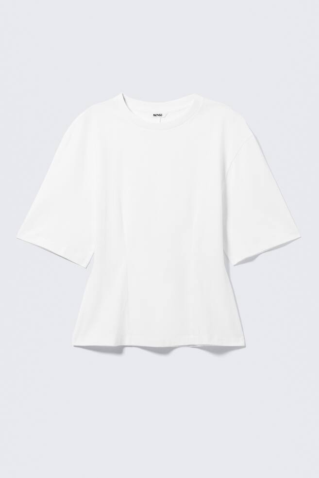 Una camiseta blanca de corte holgado presenta su vista FRONTAL, con cuello redondo, mangas anchas hasta el codo y una sutil costura vertical que recorre el frente, formando una suave silueta en línea A hacia el dobladillo recto. - 1