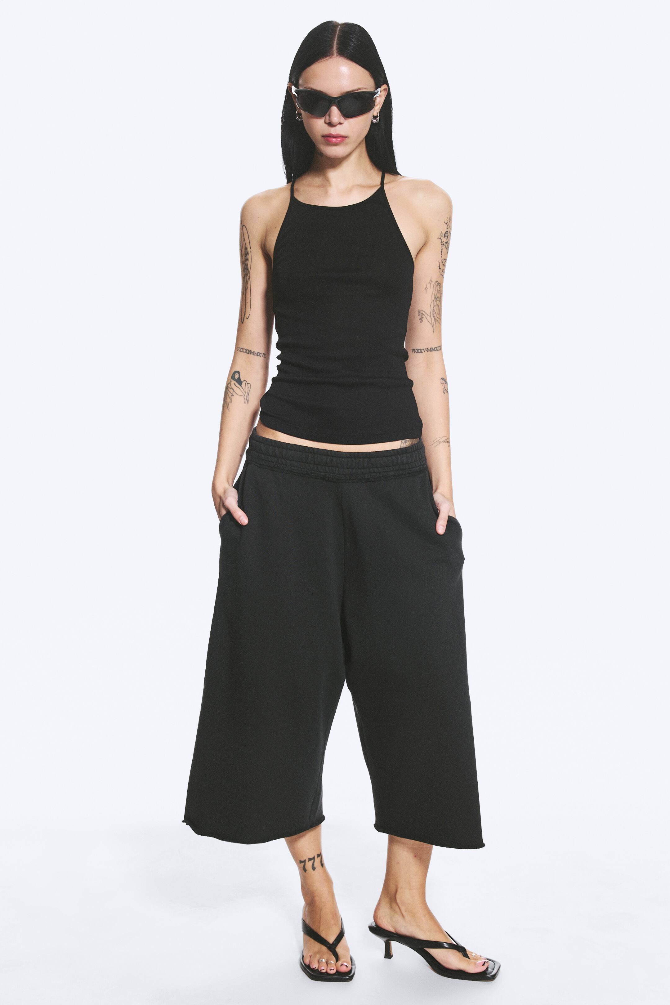 Agrandir l'image: Le pantalon de jogging noir coupe culotte présente un design à jambes larges et raccourcies avec une taille élastiquée et froncée. Il comprend des poches latérales visibles et des ourlets à coupe brute, offrant une coupe décontractée.