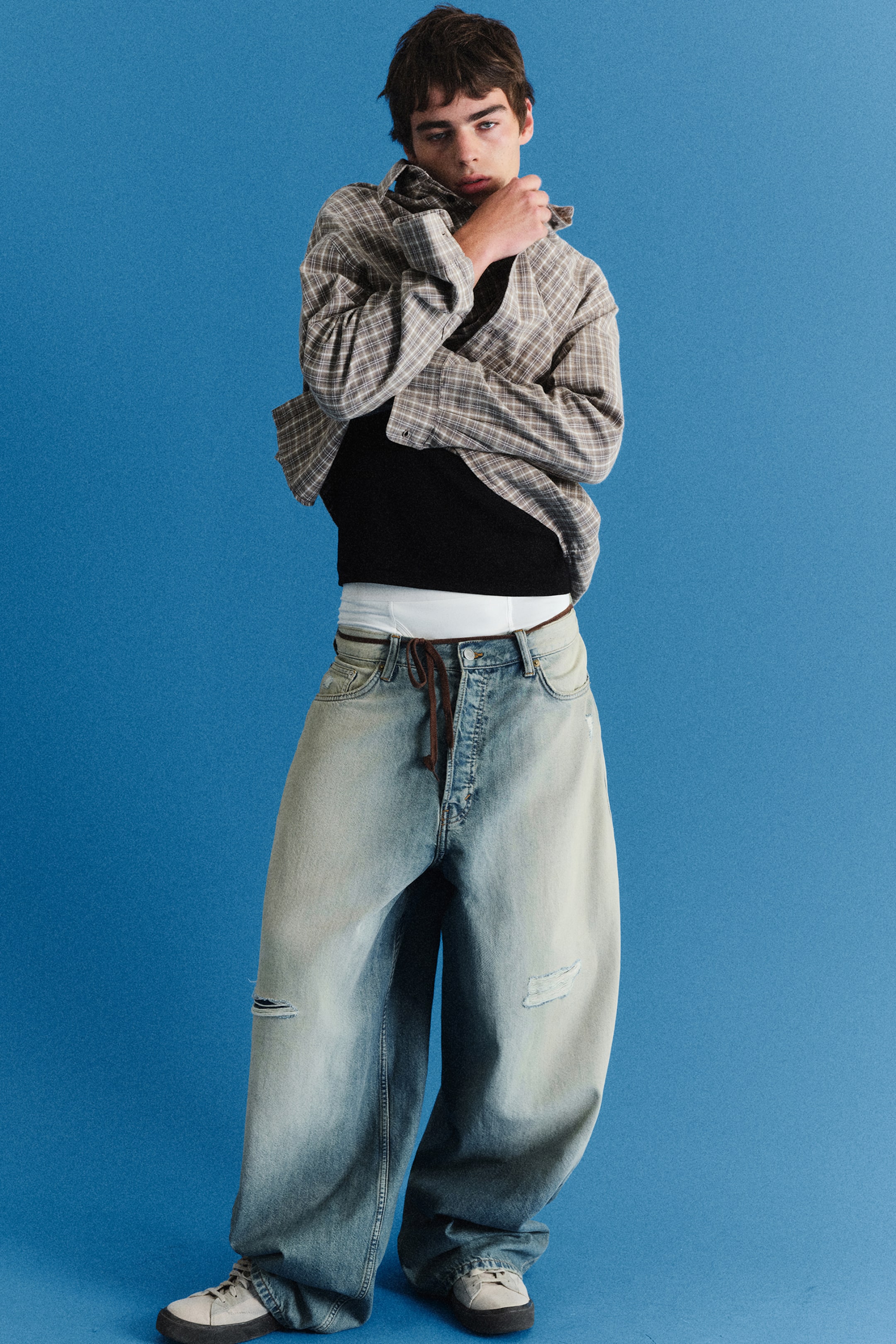 Ver imagen más grande: Los jeans baggy de tiro bajo VOID aparecen en una vista frontal, mostrando un denim azul lavado claro desteñido con una silueta oversize y holgada que cae sobre las zapatillas. Presentan una cintura de tiro bajo estilizada con un fino cinturón de cordón marrón y sutiles roturas desgastadas en las perneras, mientras se sitúan bajos para dejar ver una cinturilla blanca.
