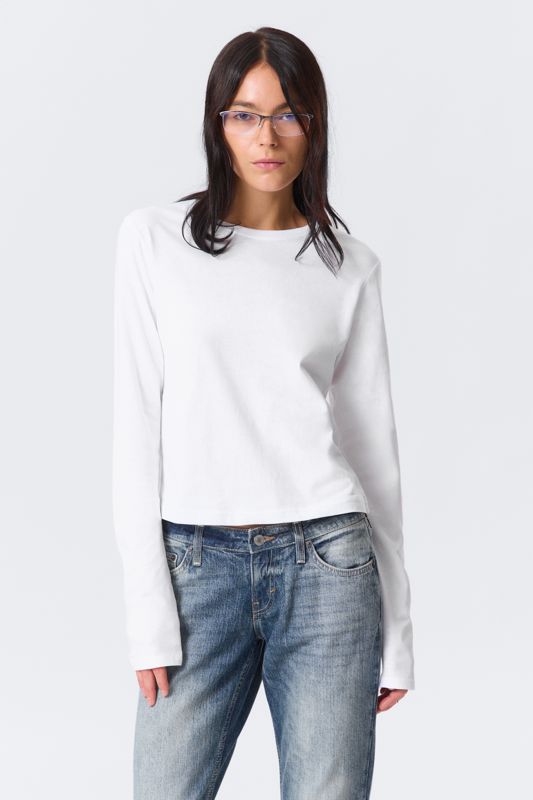 View larger image: A white long-sleeved top is featuring a crew neck and long, plain sleeves, presenting a slightly relaxed, cropped fit from a front-facing angle.