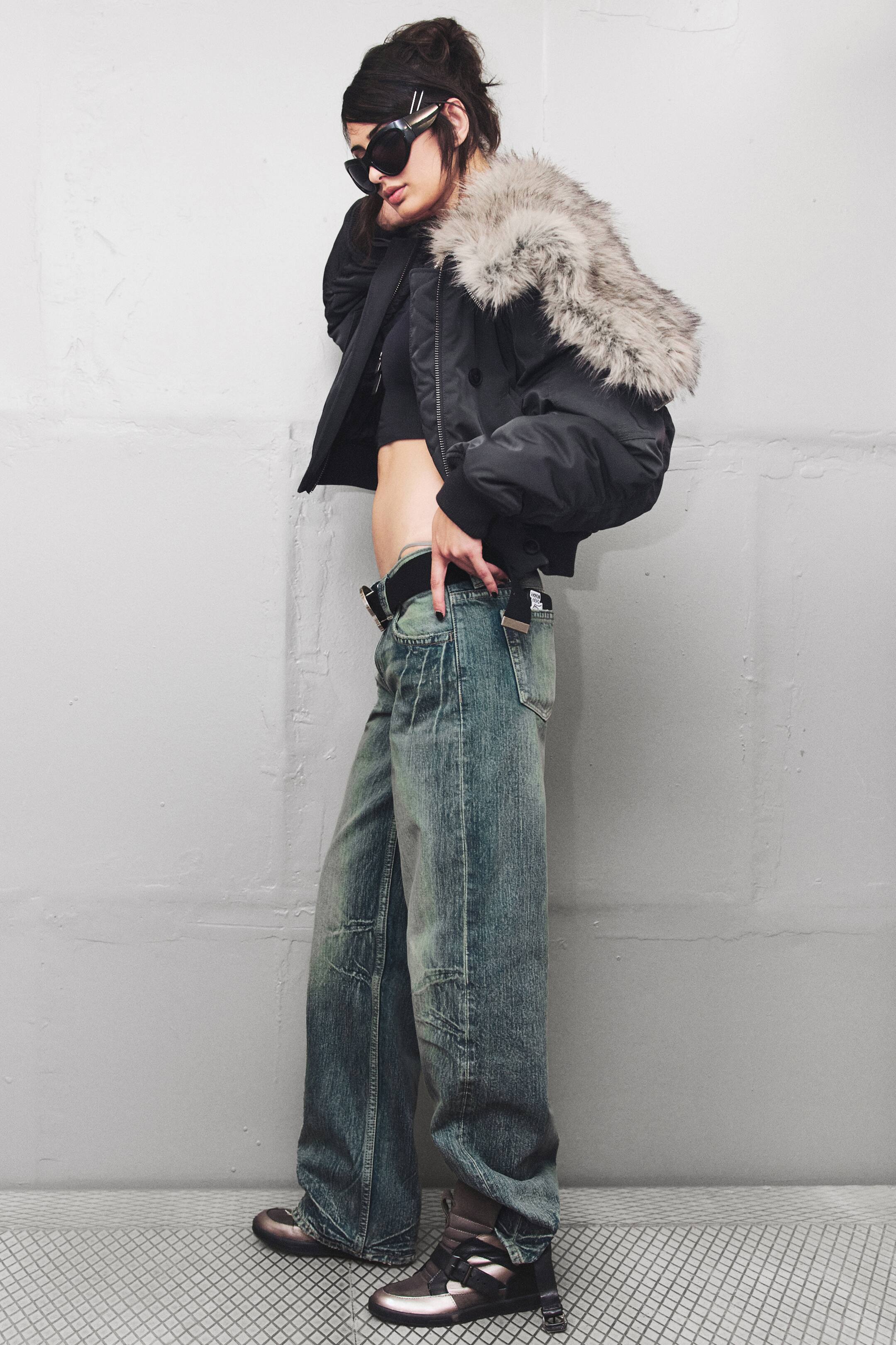 Agrandir l'image: Ces jeans taille basse à jambe droite, dans un délavage denim vert-bleu teinté, sont présentés de profil, mettant en valeur leur coupe ample et longue qui tombe sur les chaussures. Ils présentent un design classique à cinq poches et une taille basse soulignée par une ceinture noire pour accentuer la coupe low-rise.